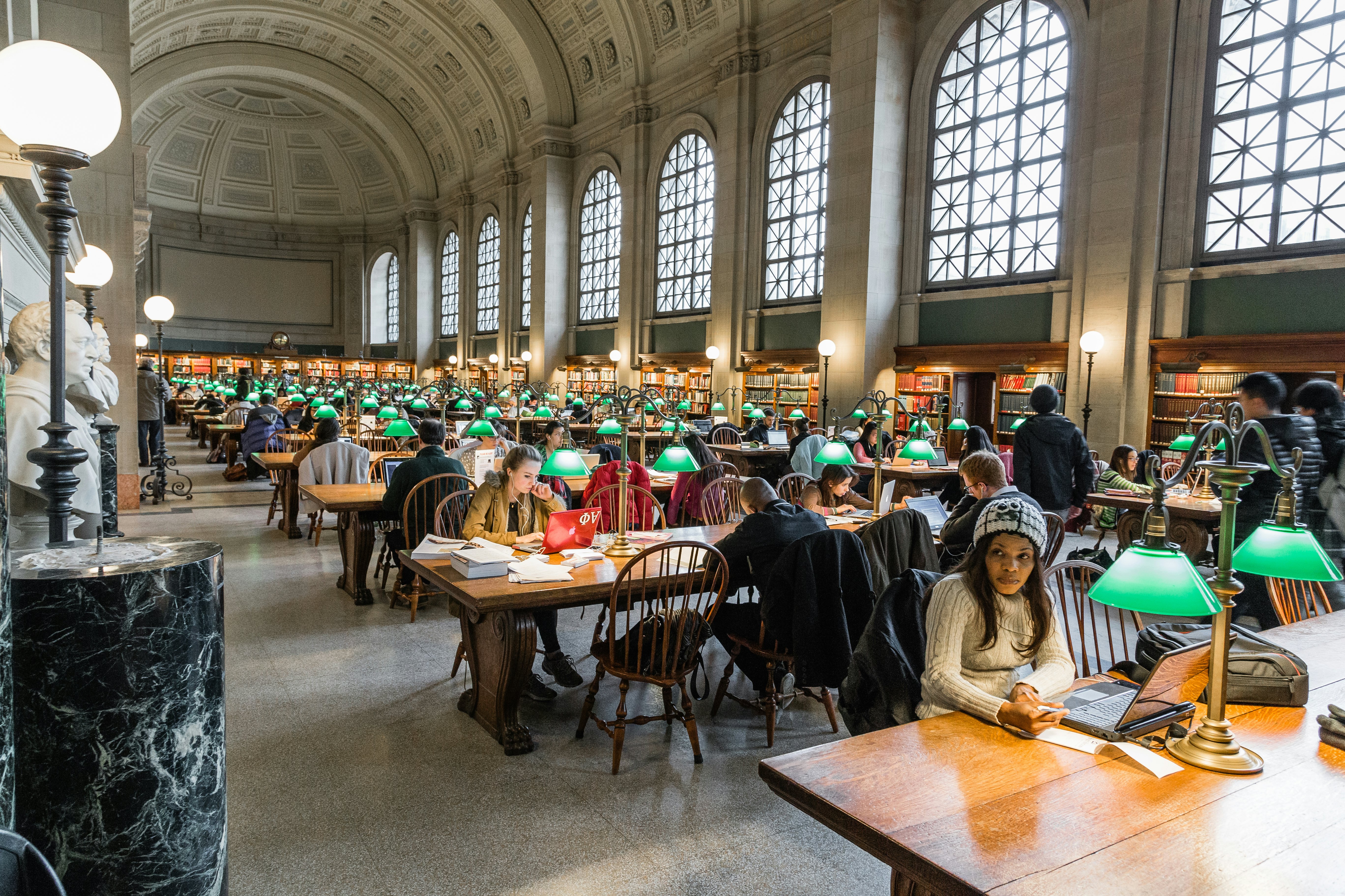 A room within Boston Public Library that has rows of desks with people quietly reading at them