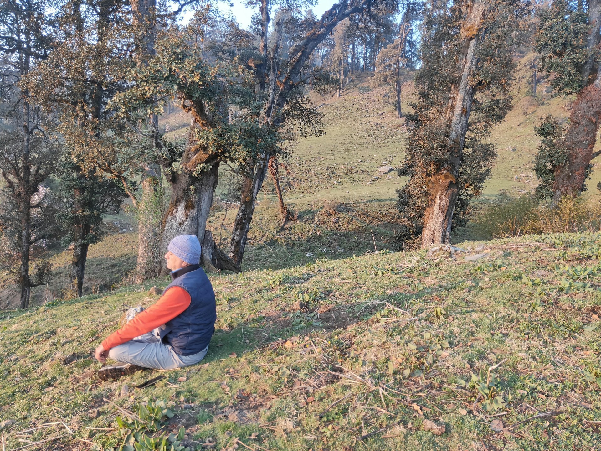 A man sits in a lotus pose on a hillside during a trek in Uttarakhand, India