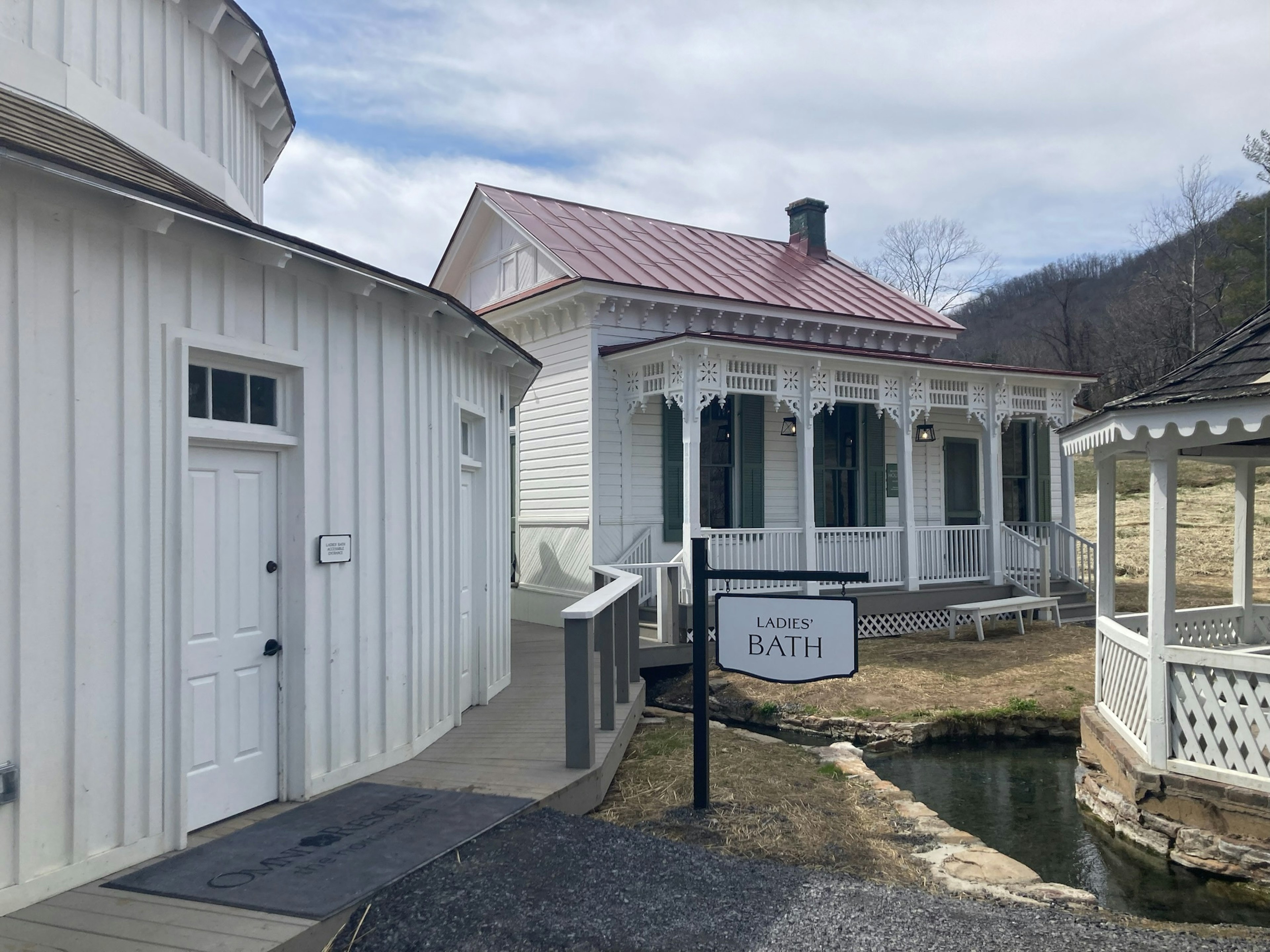 The exterior of the Ladies' Bath, a white wooden building next to a small stream