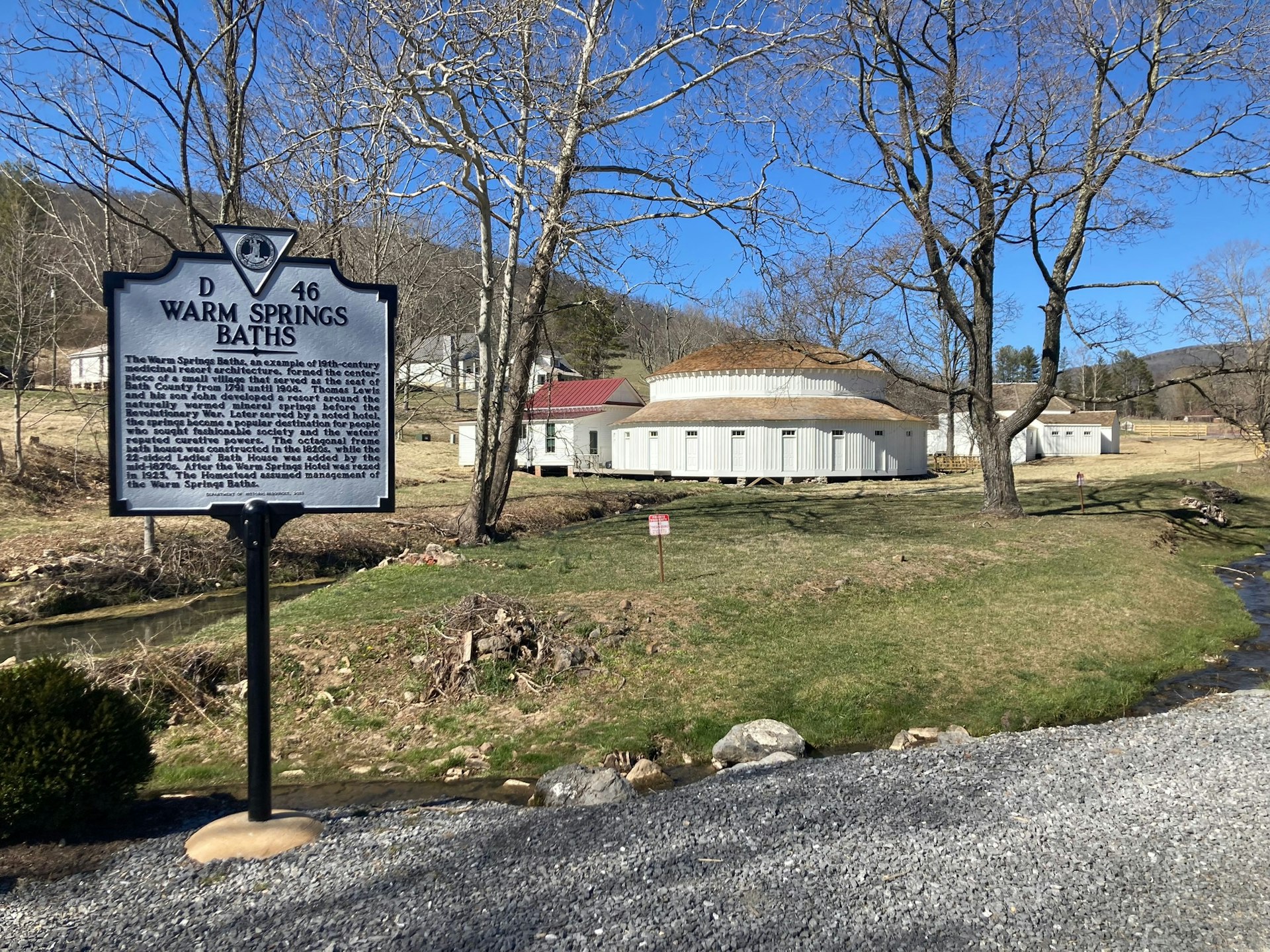 A large white circular bathhouse with a sign explaining the history of the bathhouse 