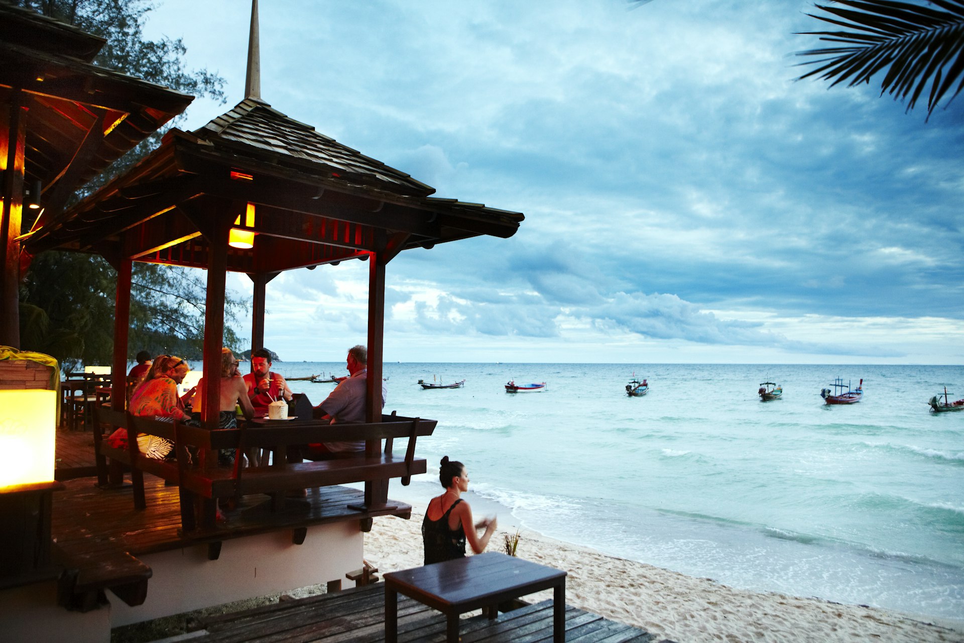 People sit in a beach deck on a Thai island. 