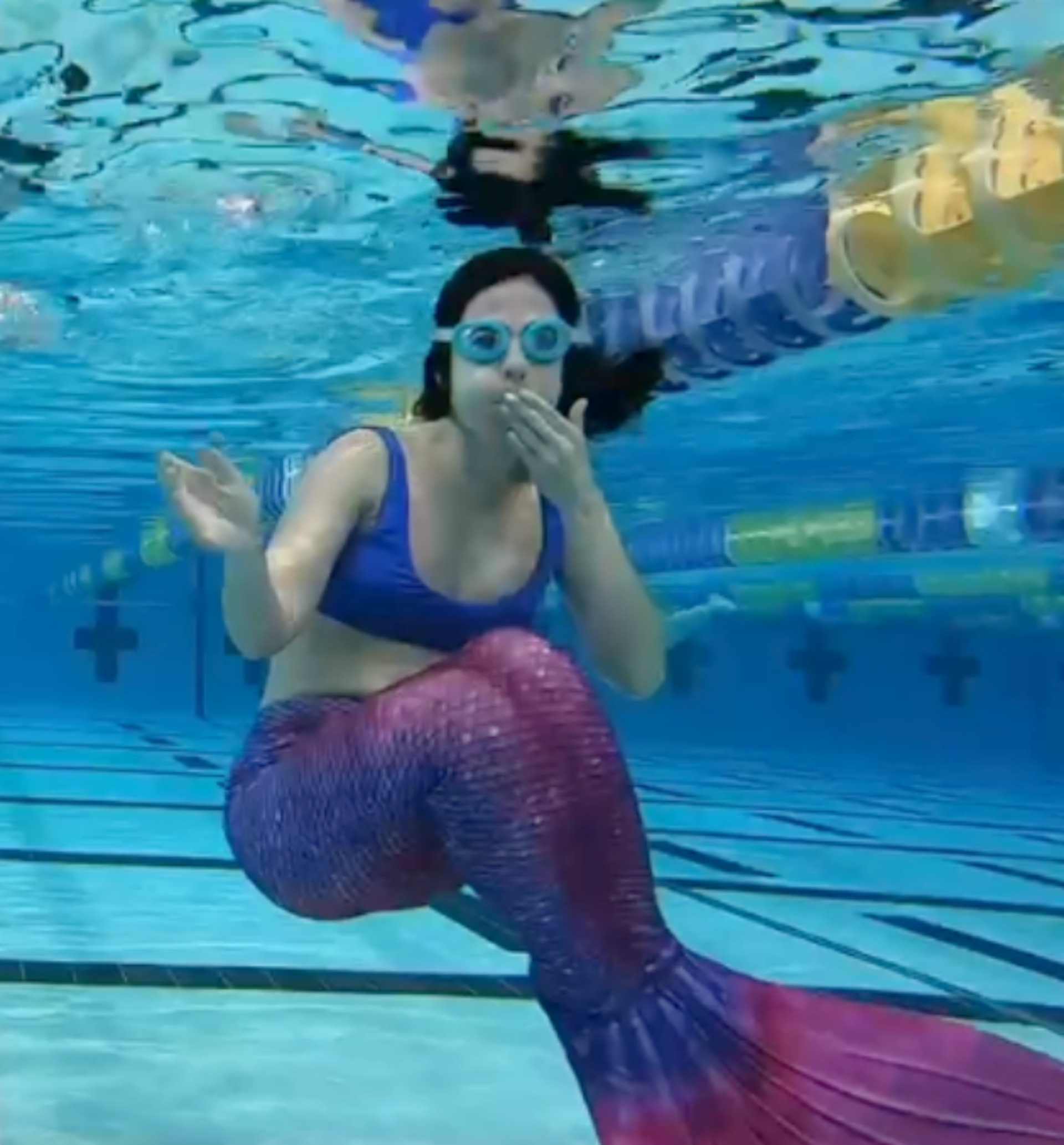 The writer in full mermaiding gear is underwater at a swimming pool with Googles on, trying the hobby for the first time