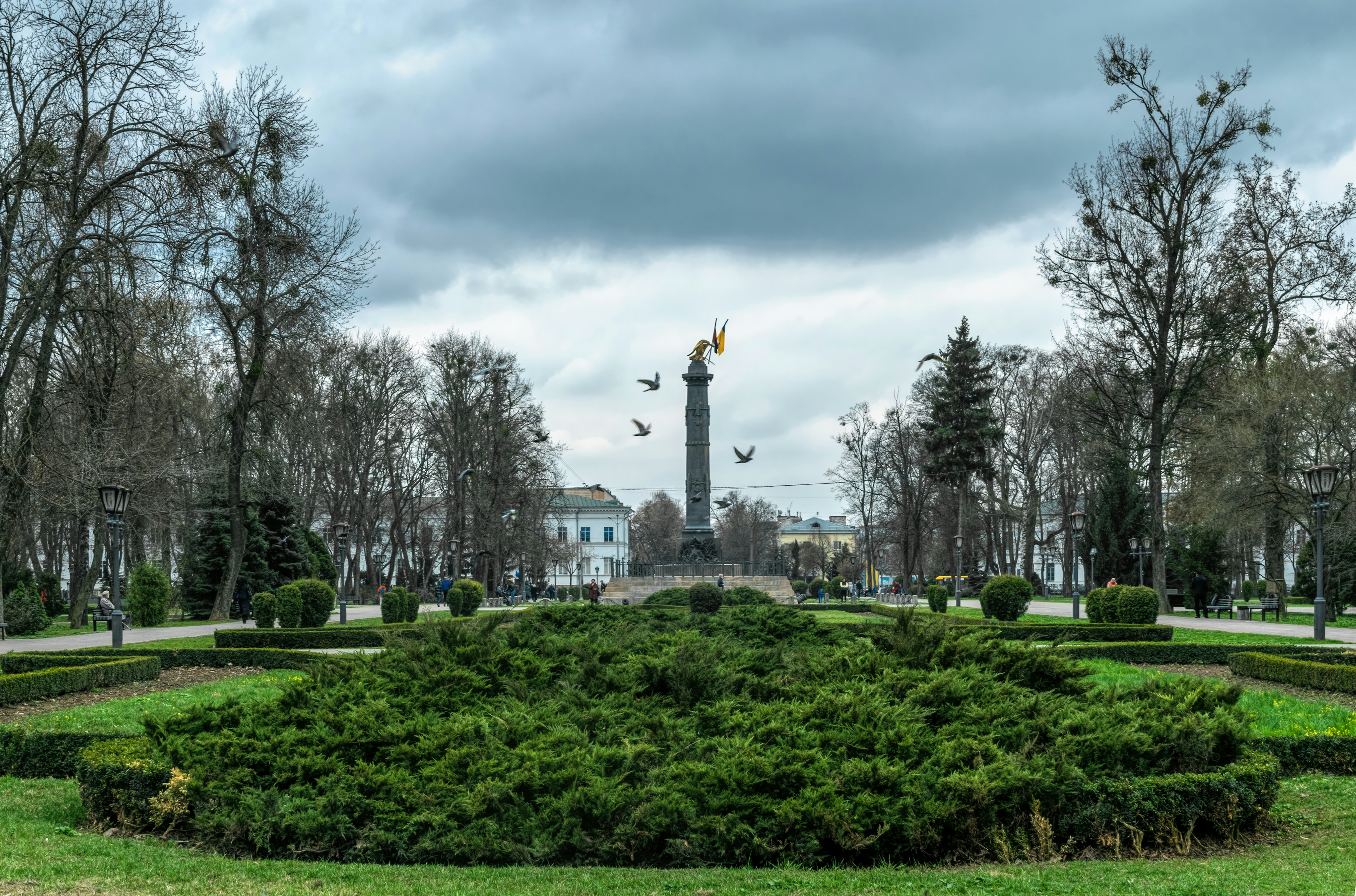Memorial column with the national flags of Ukraine and green flower beds of the city park, Korpusny Park in Poltava, Ukraine.
