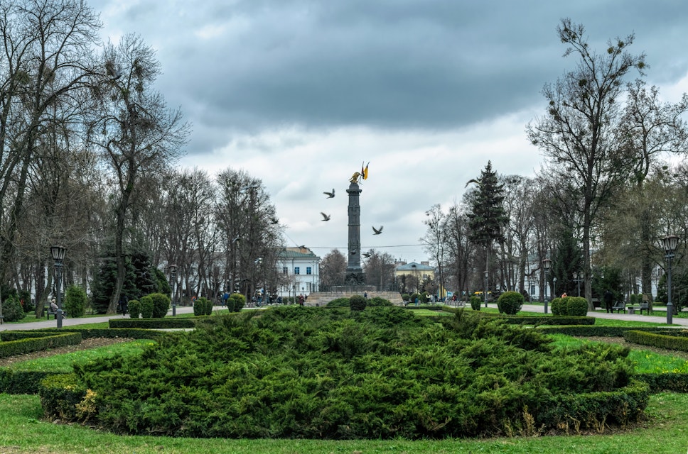 Memorial column with the national flags of Ukraine and green flower beds of the city park, Korpusny Park in Poltava, Ukraine. 