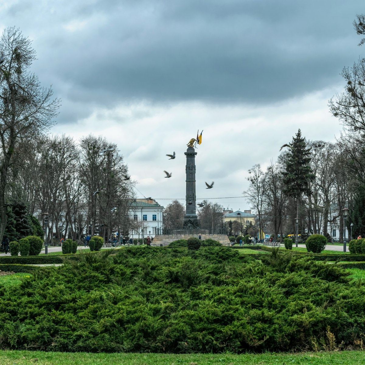Memorial column with the national flags of Ukraine and green flower beds of the city park, Korpusny Park in Poltava, Ukraine. 