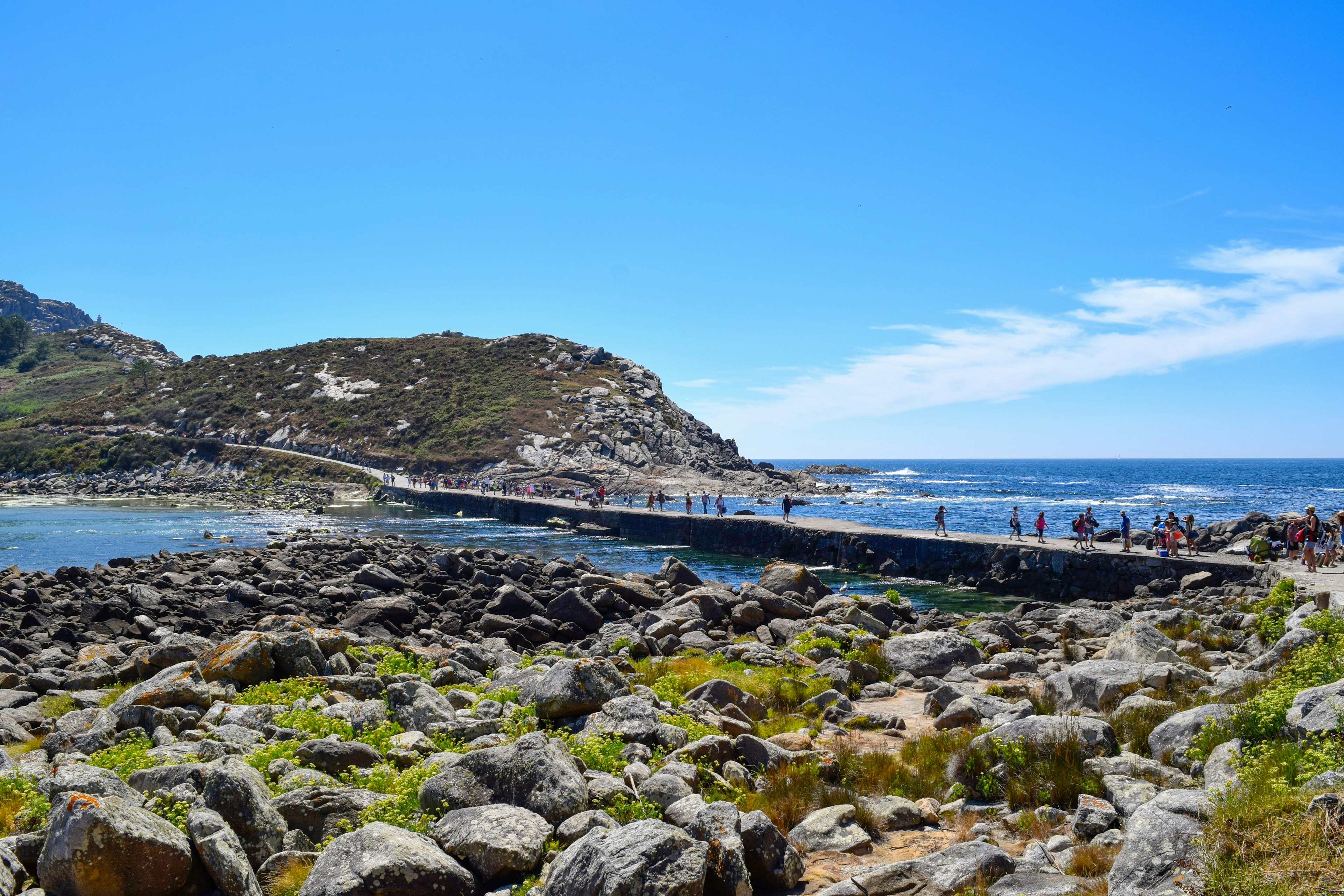 People walk along a walkway just above sea level that connects two rocky islands