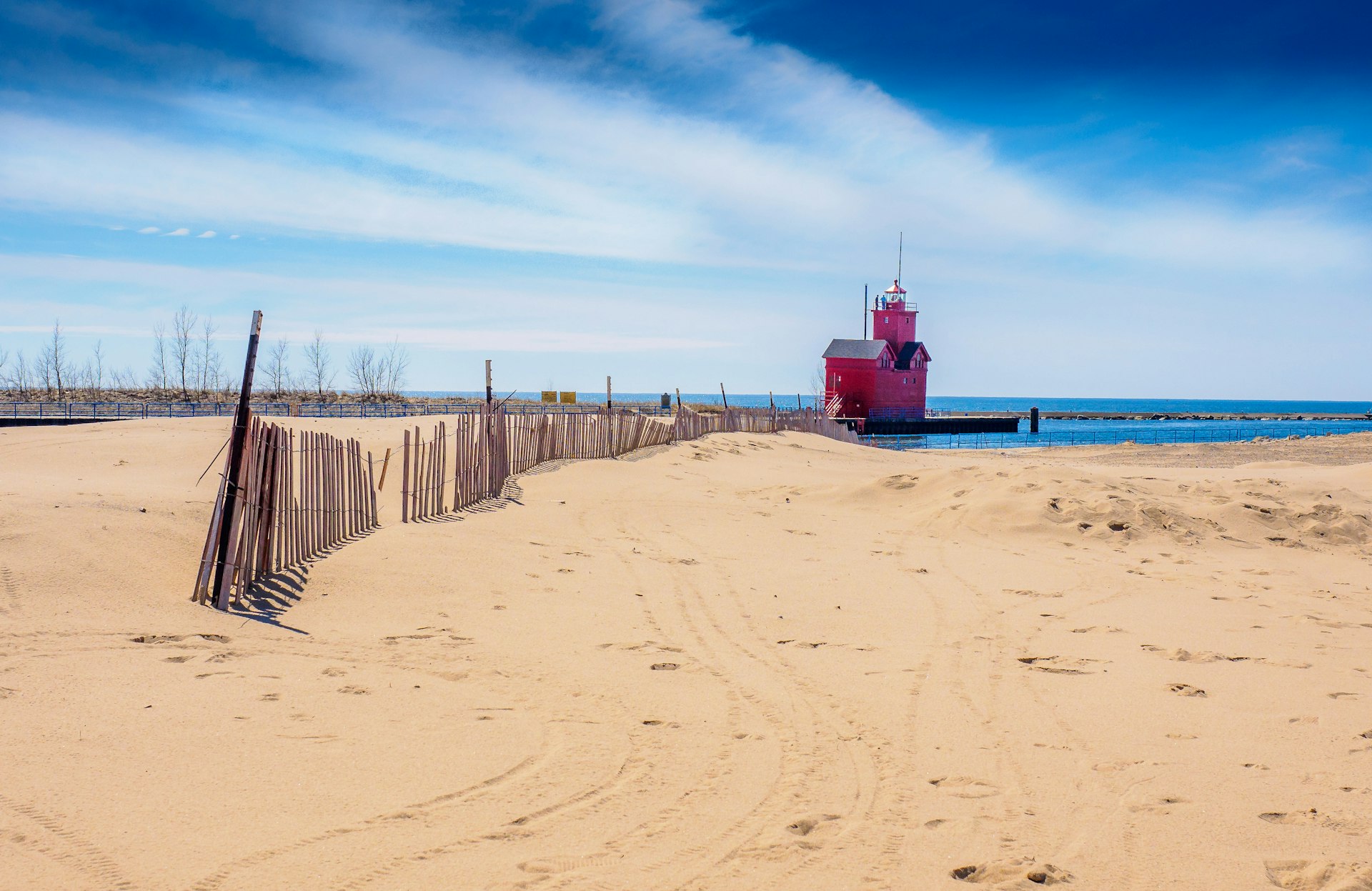 A wide sand beach with a fence and a big red lighthouse in the distance