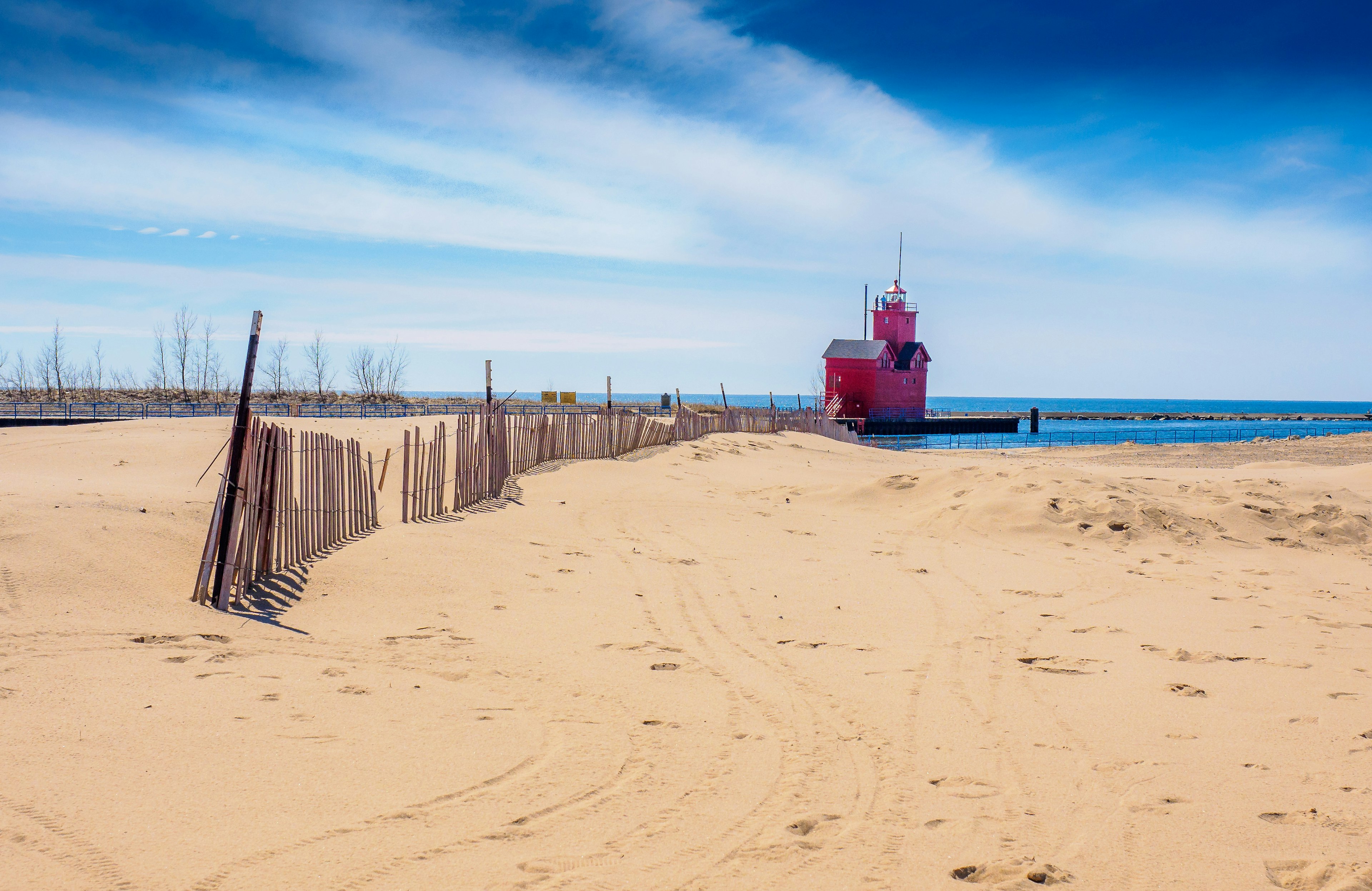 A wide sand beach with a fence and a big red lighthouse in the distance