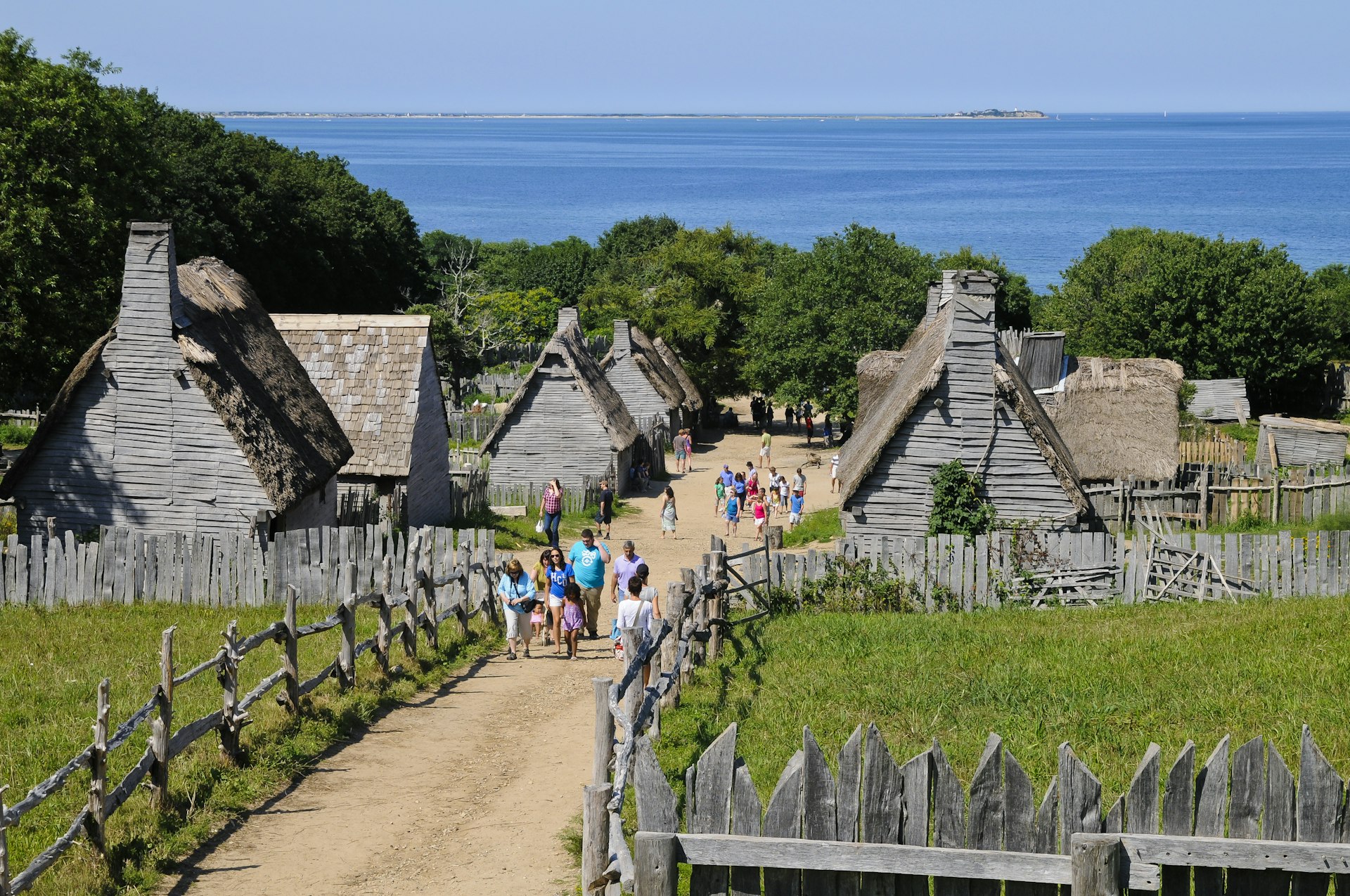 A village of small wooden houses by the sea with tourists wandering among them 