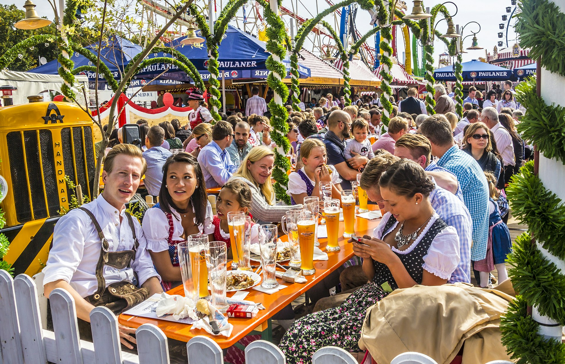 People dressed in traditional costumes are sitting at long wooden tables in a beer garden.