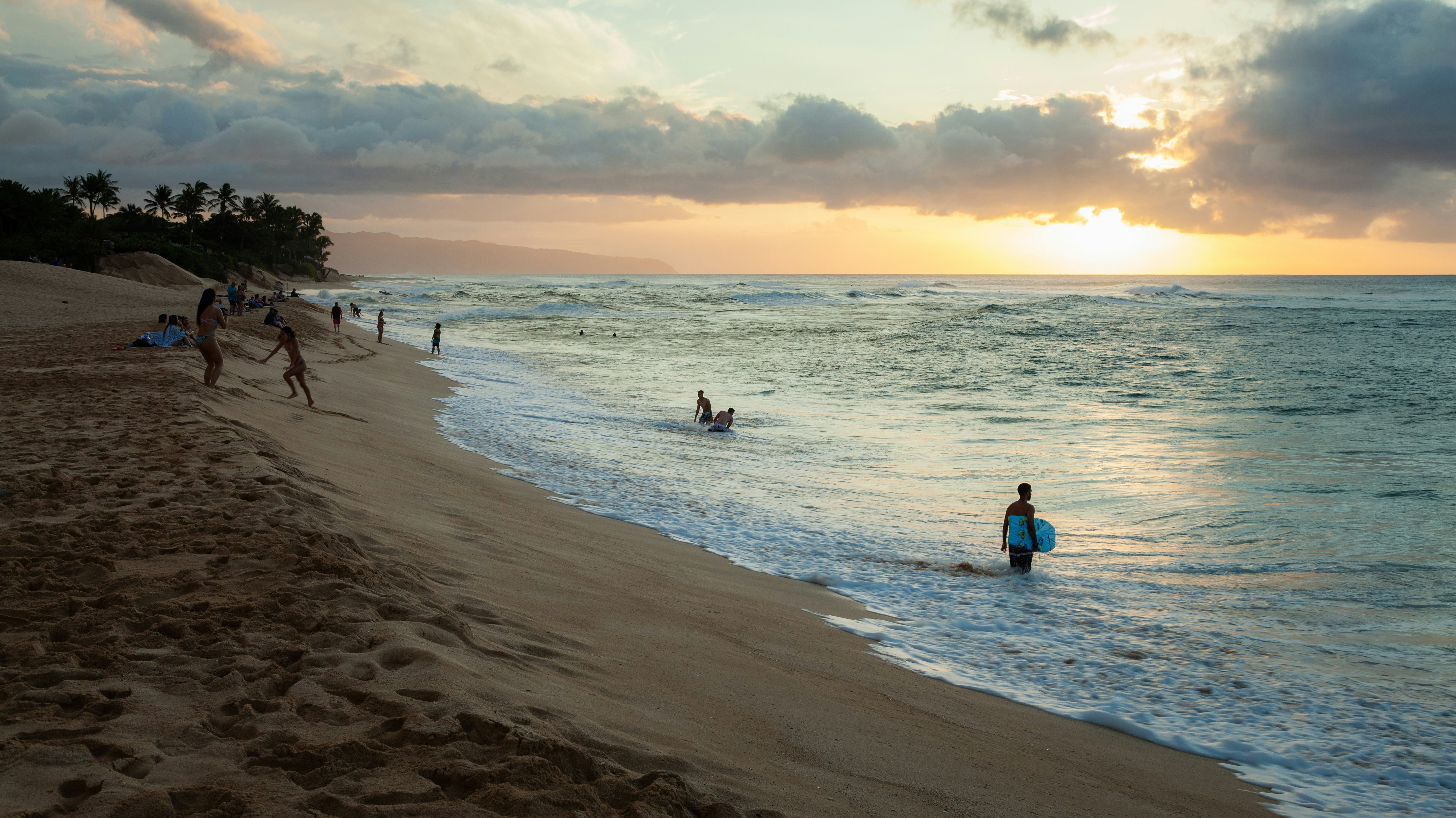 Seascape of sunset and beach with silhouettes of surfers and people swimming.