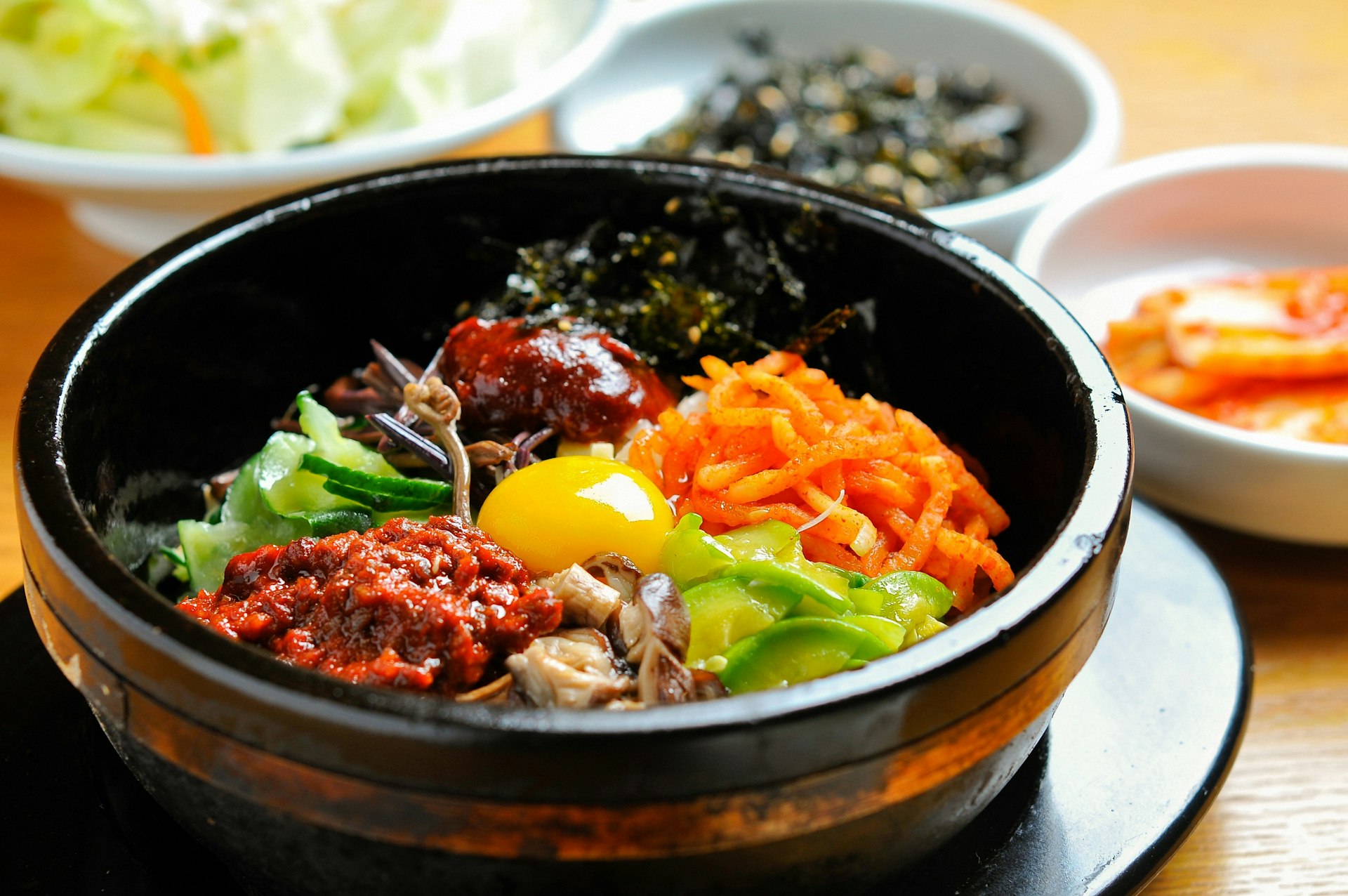 A stone bowl is full of mixed vegetables and an egg in a Korean bibimbap. 