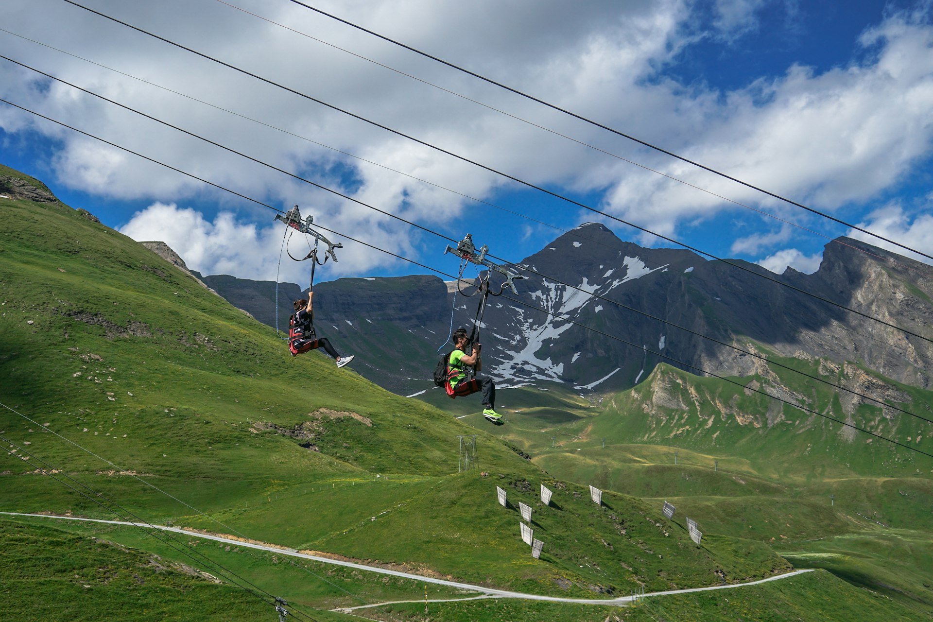 Two people on a zip line fly down a cable in a very moutainous area