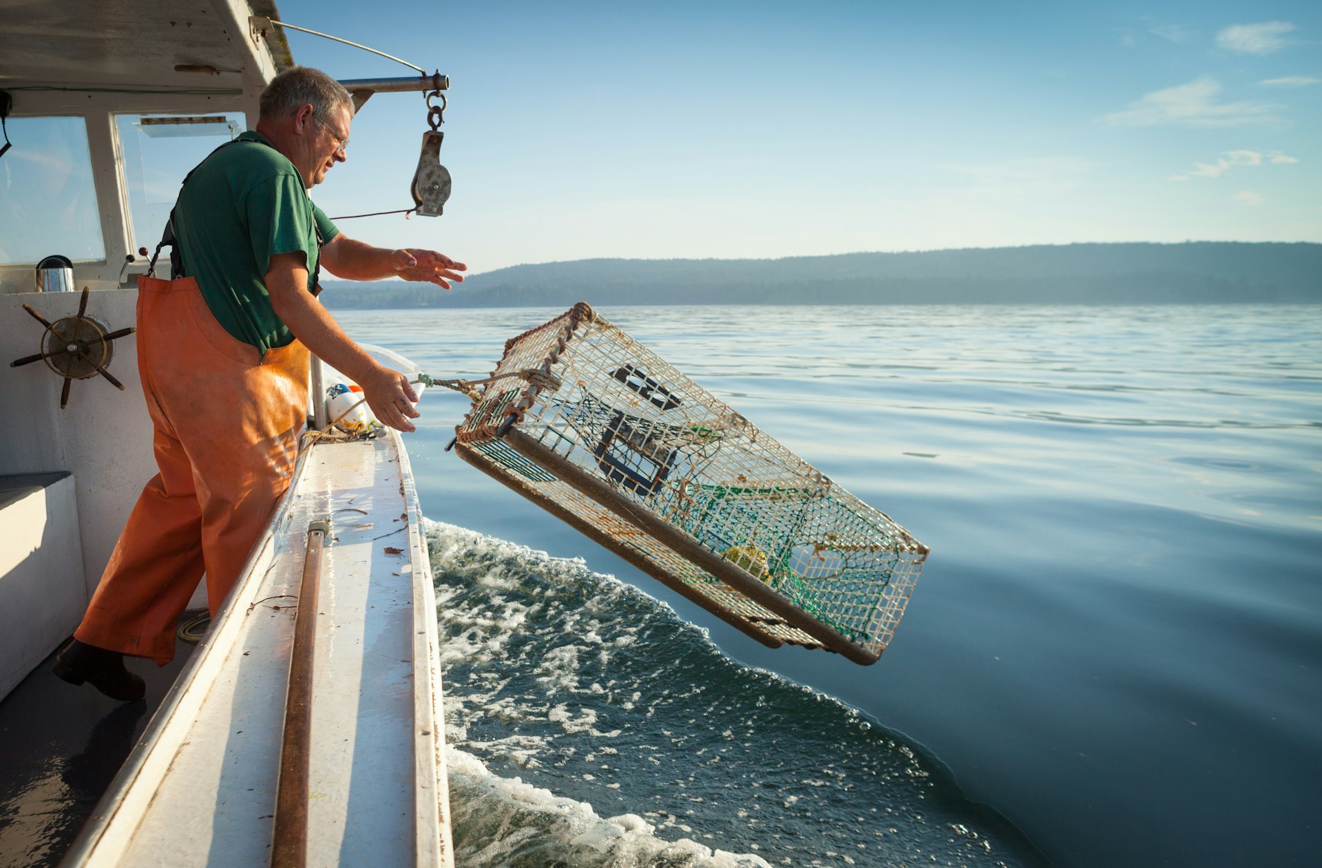 A man throws a lobster cage off the side of a boat out at sea near the Maine coast