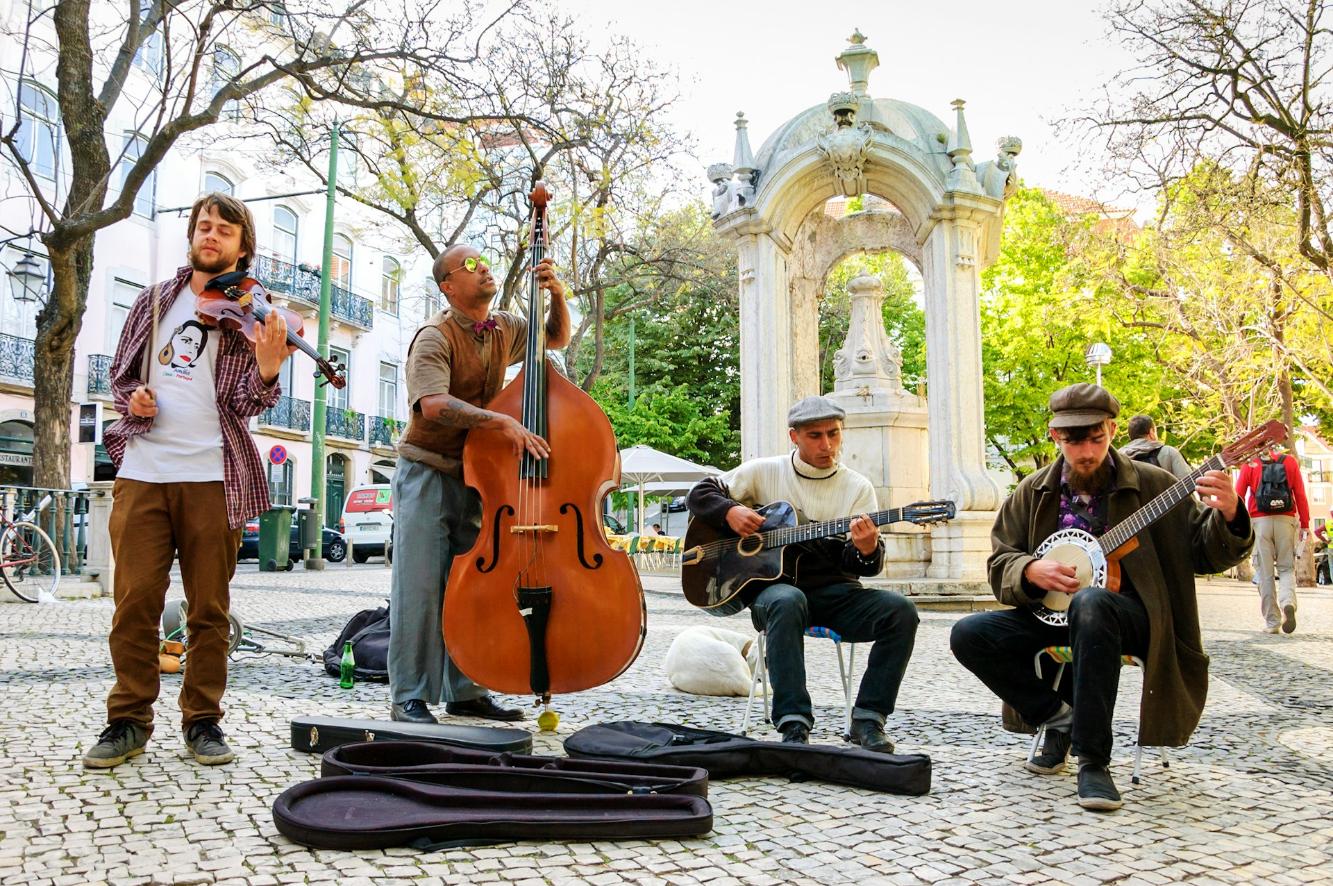 Four musicians play folk music on stringed instruments in a public square in Lisbon