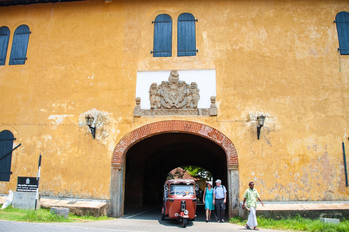 Tuk tuk drives through the entrance of the old Dutch gate with British Coat of Arms above.