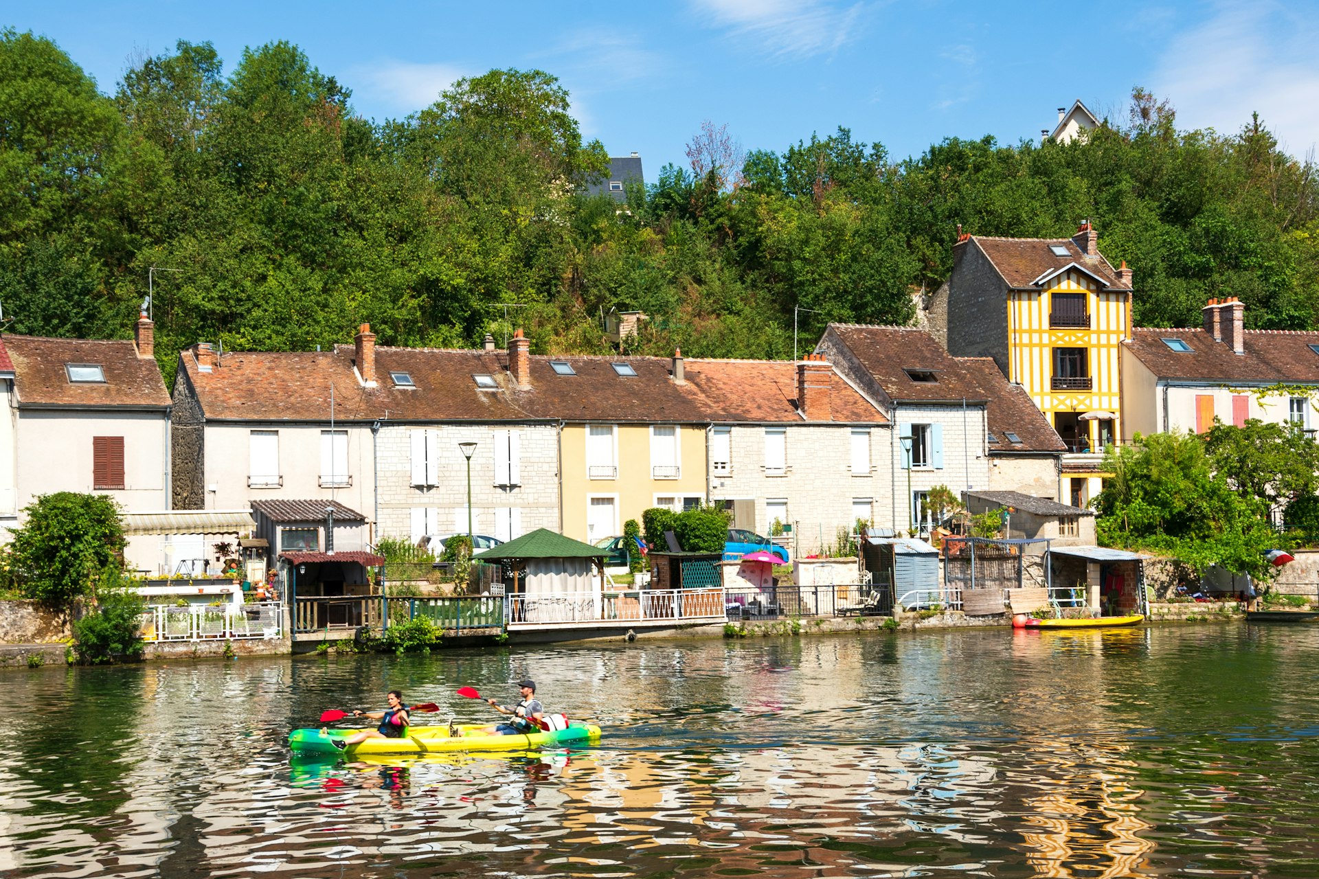 Couple paddling a kayak on the Loing river with picturesque houses in the background. Nemours is a medieval town in at Seine-et-Marne department of Ile-de-France.
