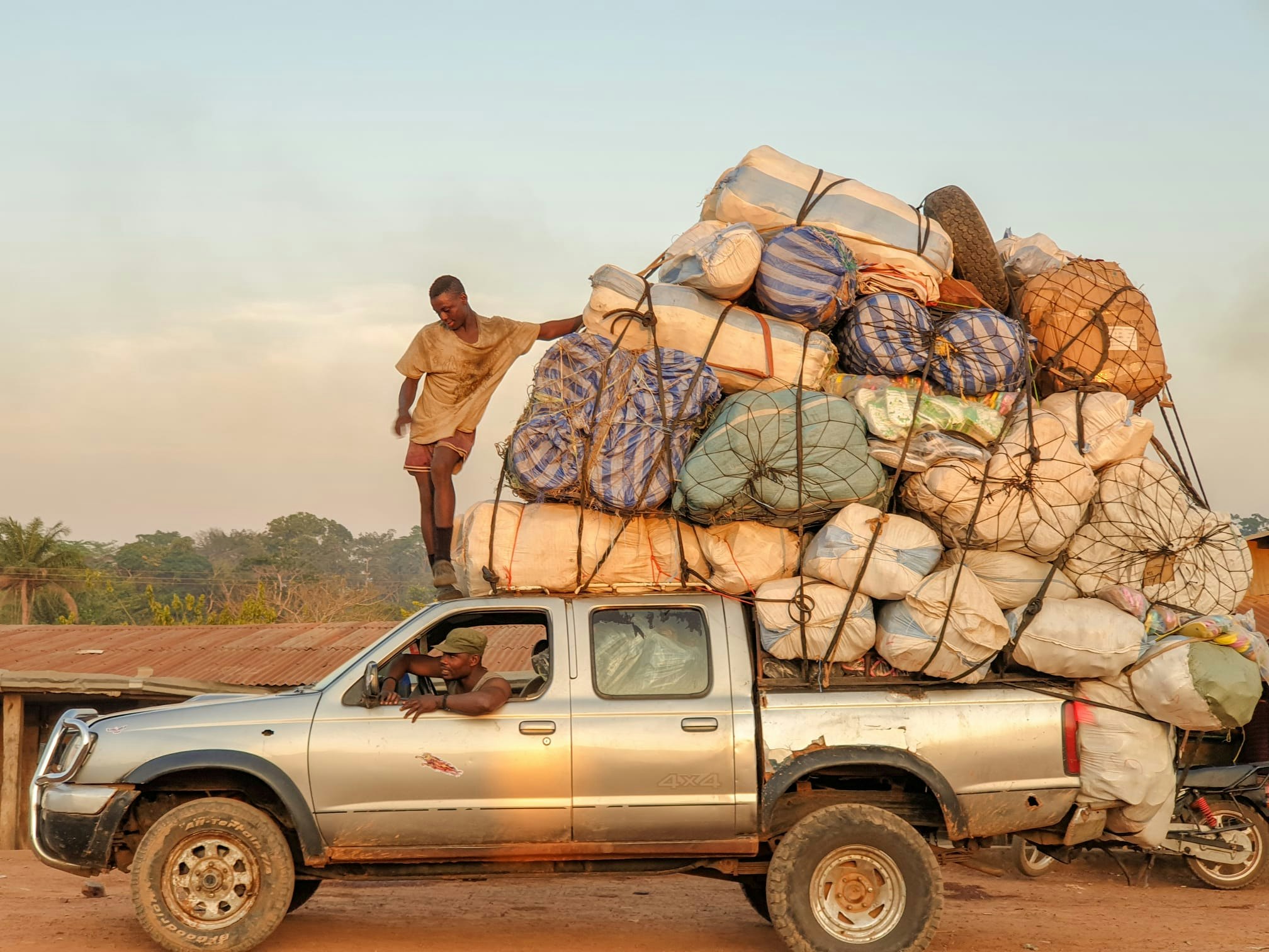 A young man stands on top of a truck with cargo. 