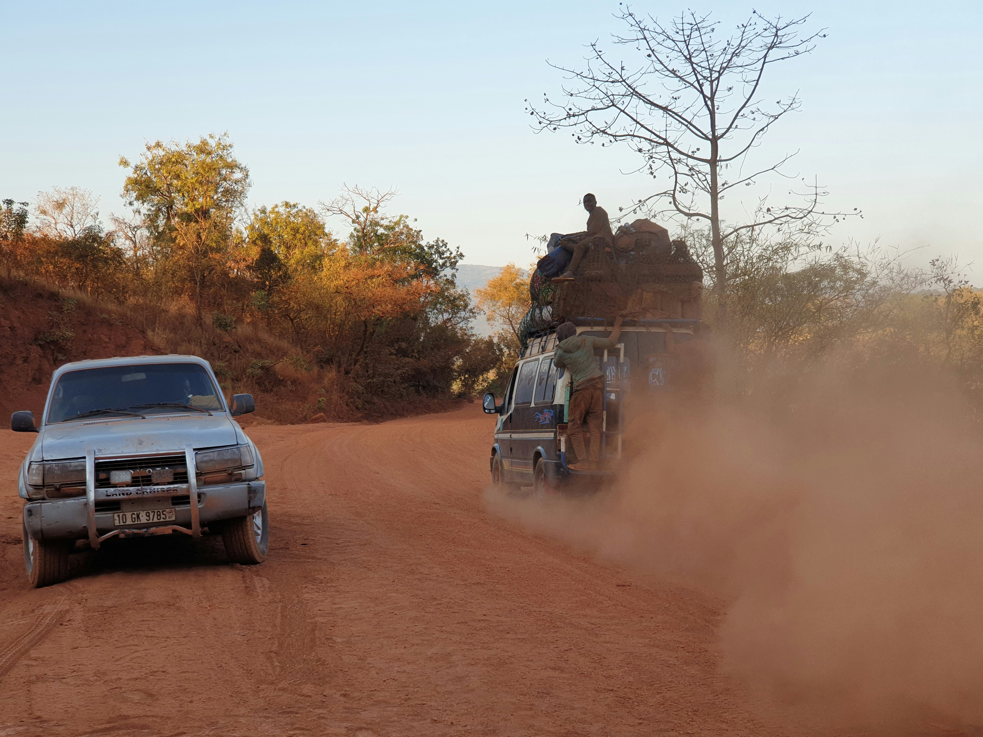 A car sits on the side of the red dusty road in West Africa. 