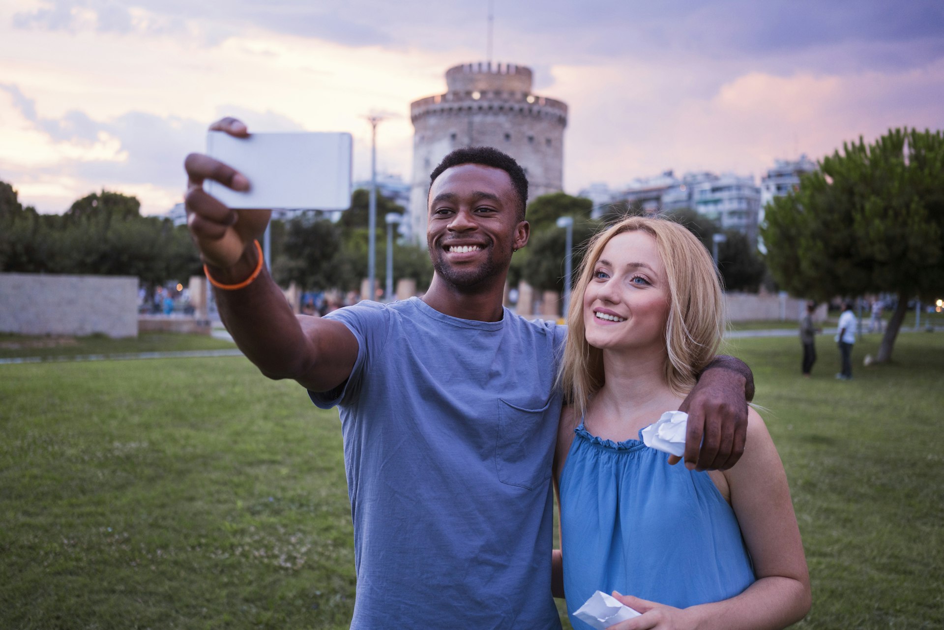 Couple walking through town together at night and take a selfie in front of the white tower in Thessaloniki