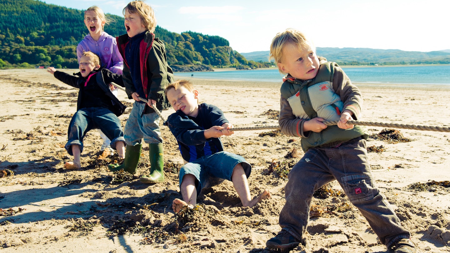 Five children playing Tug of War with a rope on the beach.
113740347