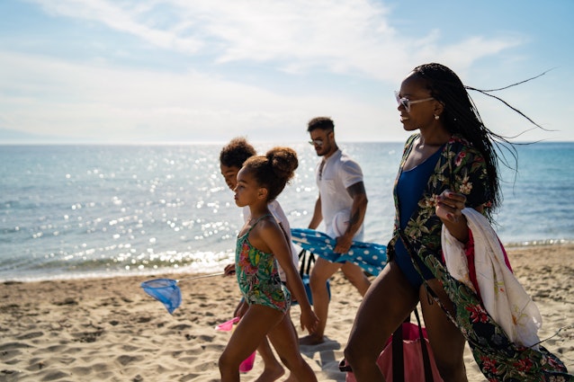 Children and their parents are walking on the beach and carrying parasol and other beach stuffs.
1157800361
A family with two kids walking along the beach in Greece together