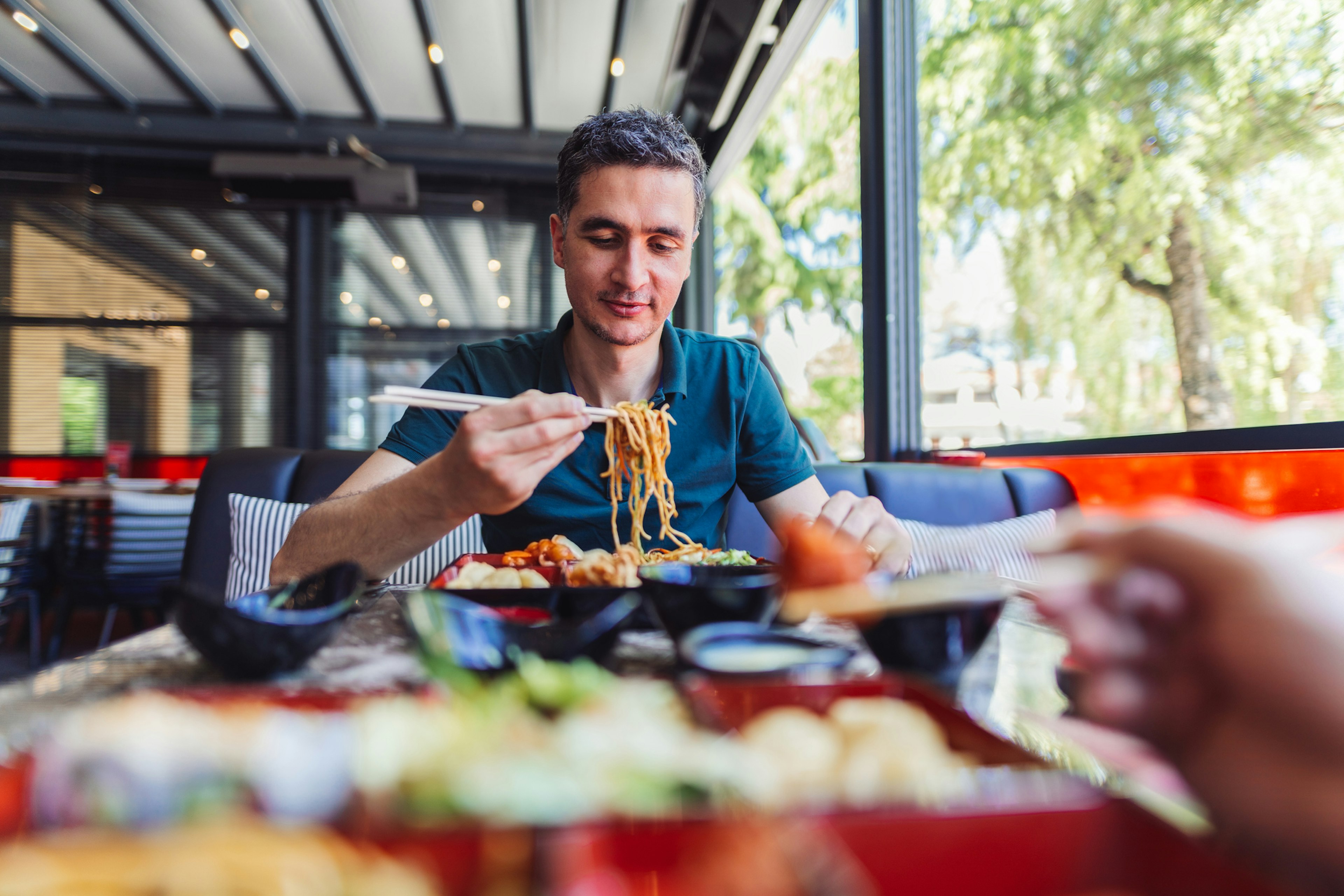 A man eating noodles with chopsticks in a restaurant