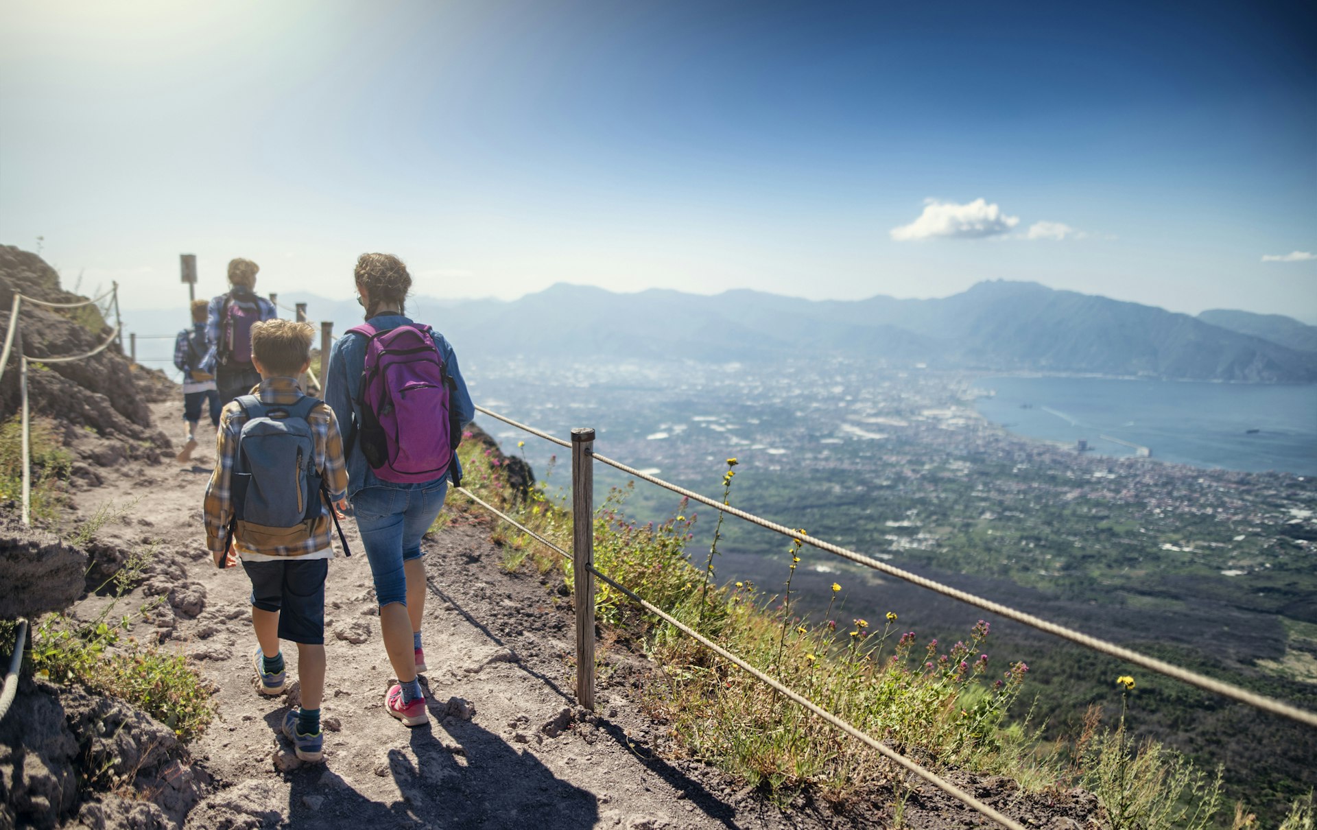 Family walking on the summit of Mount Vesuvius volcano with a view down towards the sea of Naples Bay