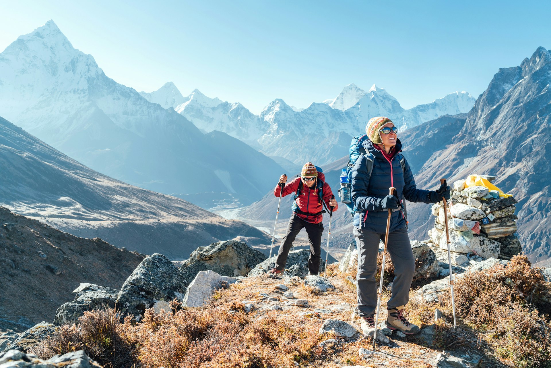 A couple with trekking poles and backpacks follow a trail through the mountains