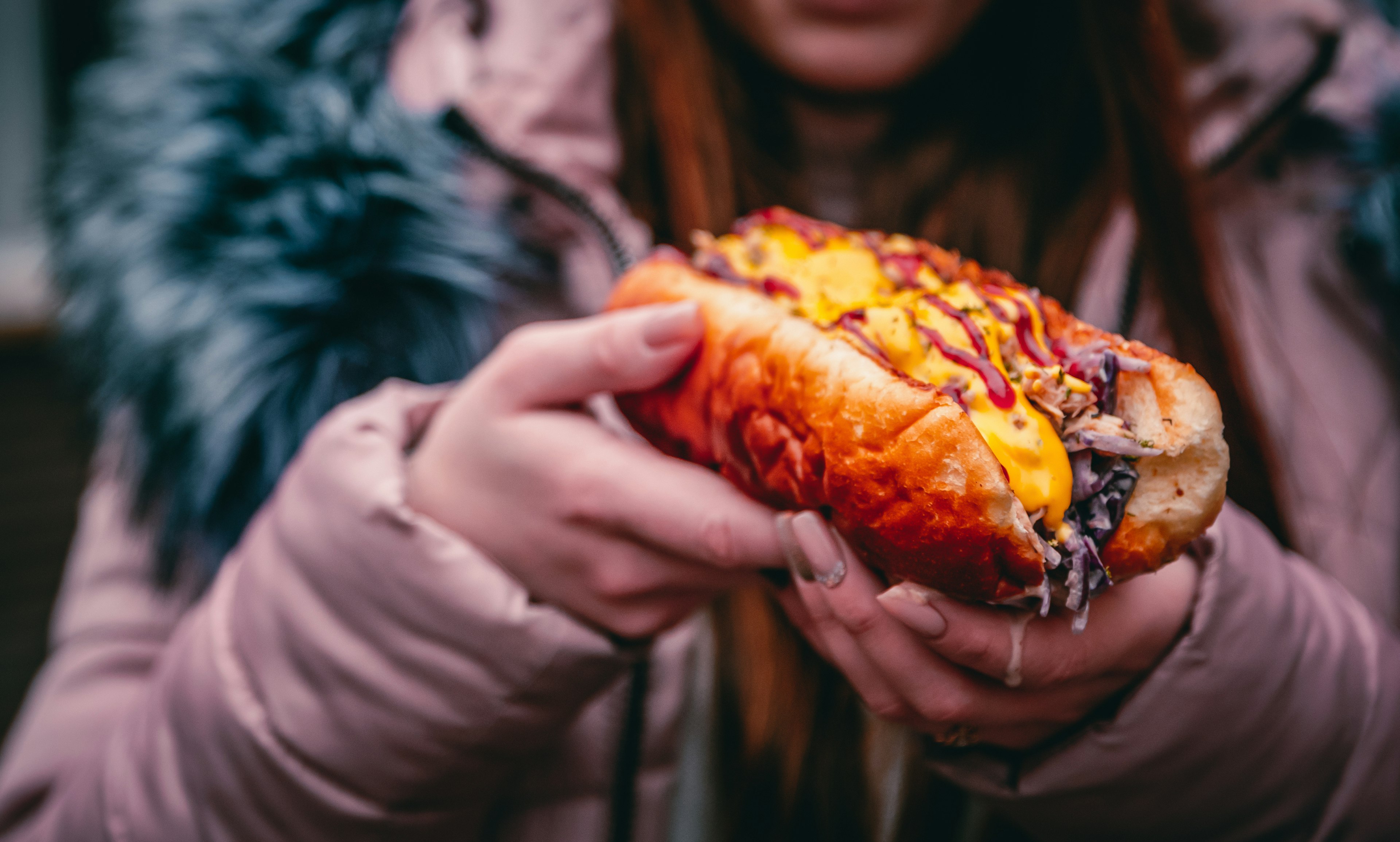 Philly cheese steak sandwich with meat, vegetables, cheese and sause in the hands of woman.