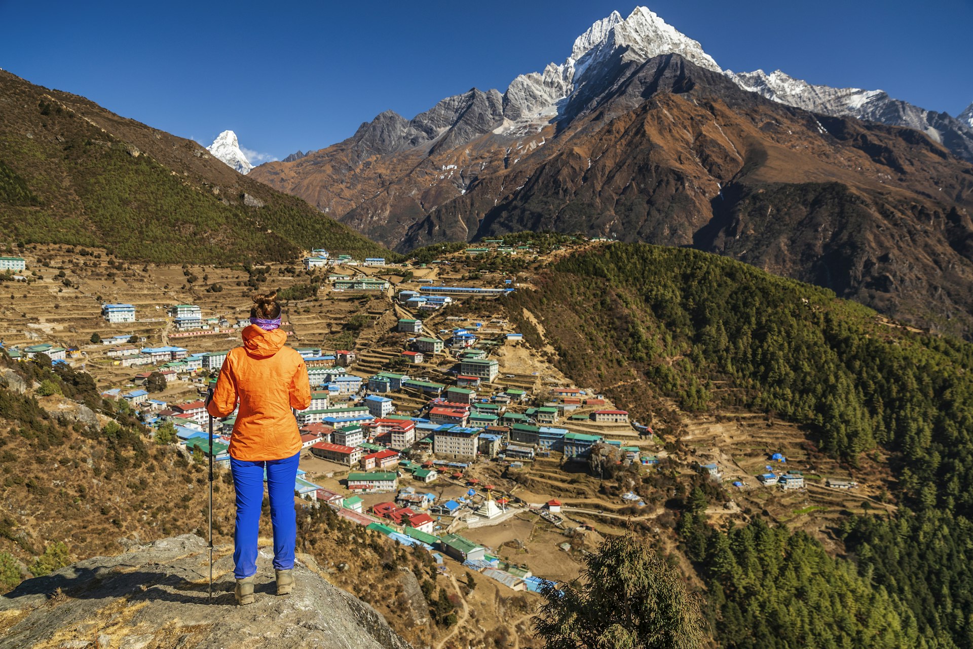 A female trekker stands on a high point looking down towards a mountain settlement