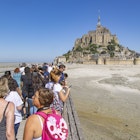 Lines of tourists and visitors waiting to board the bus towards the parking or arriving and walking towards the island. Mont-Saint-Michel tidal island with the magnificent medieval monastic buildings and the Abbey of Saint Michel with the statue of Archangel Michael atop the spire, in Normandy, France. Le Mont Saint Michel is a UNESCO World Heritage Site since 1979 and second most visited monument in France. The holy island with its breathtaking bay is a major Christian pilgrimage site destination for Europe for centuries. The Mont-Saint-Michel is one of Europes most unforgettable sights. July 2022 (Photo by Nicolas Economou/NurPhoto via Getty Images)
1242376118
brittany, world heritage, religious, wall, destinations, exterior, world, bridge, st michel, crowd, panorama, reflections, saint michel, vacation, site, attraction, michael, fortification, mont saint michel, mont st michel, historical, building, gothic, walled, landscape, bretagne, famous, unesco, mont-saint-michel, fortress