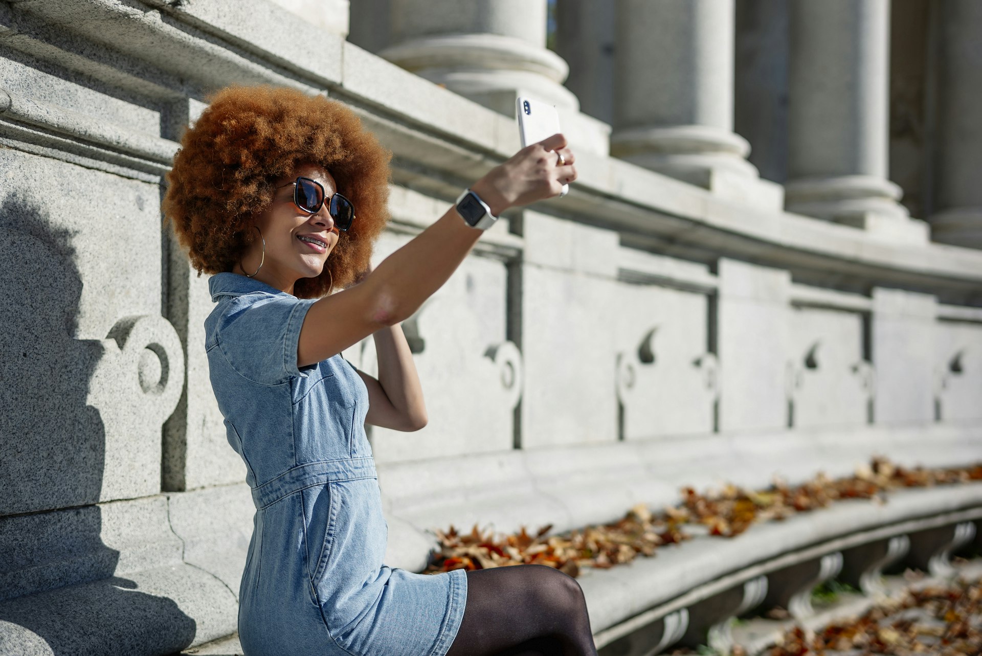 A young woman with an afro takes a selfie in the sun drenched Retiro Park in Spain