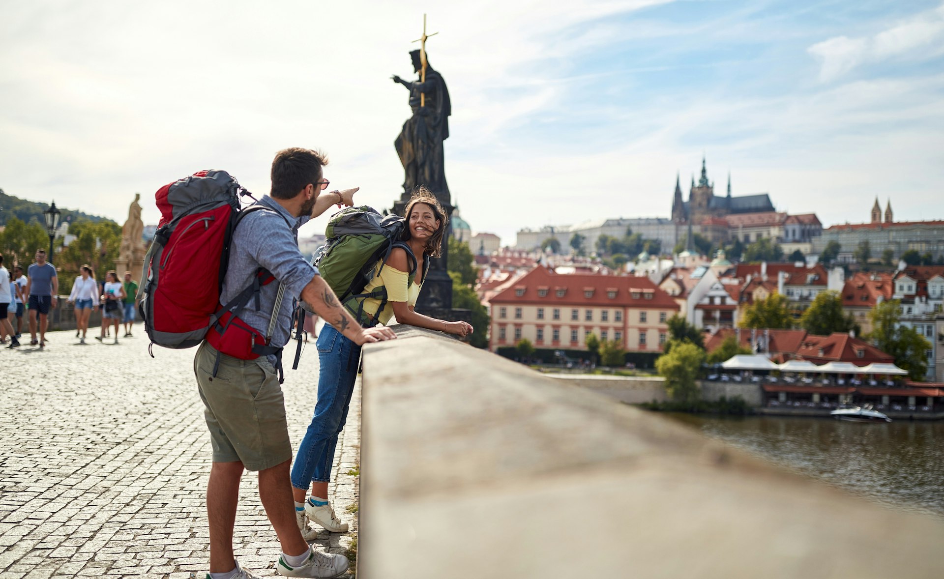 A man and woman wearing backpacks standing on a bridge in Prague in the sunshine