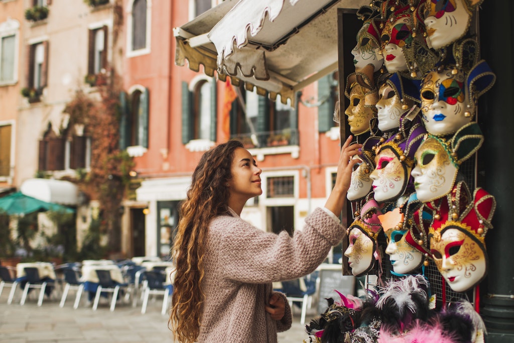 Vacations and shopping in Venice, Italy. Tourist woman want to choose and buy one. Traditional beautiful handmade carnival masks as souvenir selling on street kiosk. Giel enjoying and smiling.
1304803873
A woman looking at Venetian masks at a souvenir shop in Venice