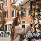 Vacations and shopping in Venice, Italy. Tourist woman want to choose and buy one. Traditional beautiful handmade carnival masks as souvenir selling on street kiosk. Giel enjoying and smiling.
1304803873
A woman looking at Venetian masks at a souvenir shop in Venice