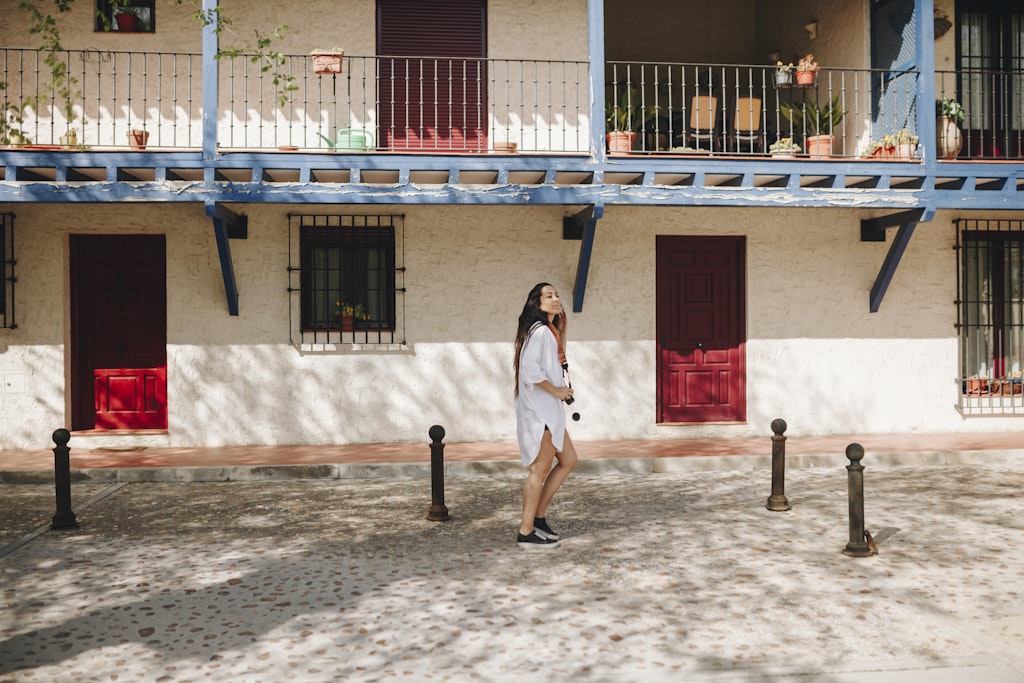 A woman with a camera around her neck strolls through a village square lined with balconies
