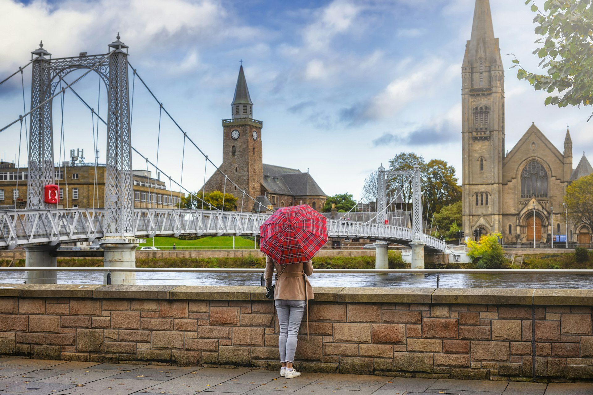 A tourist holding a red tartan umbrella stands looking at the view of a church