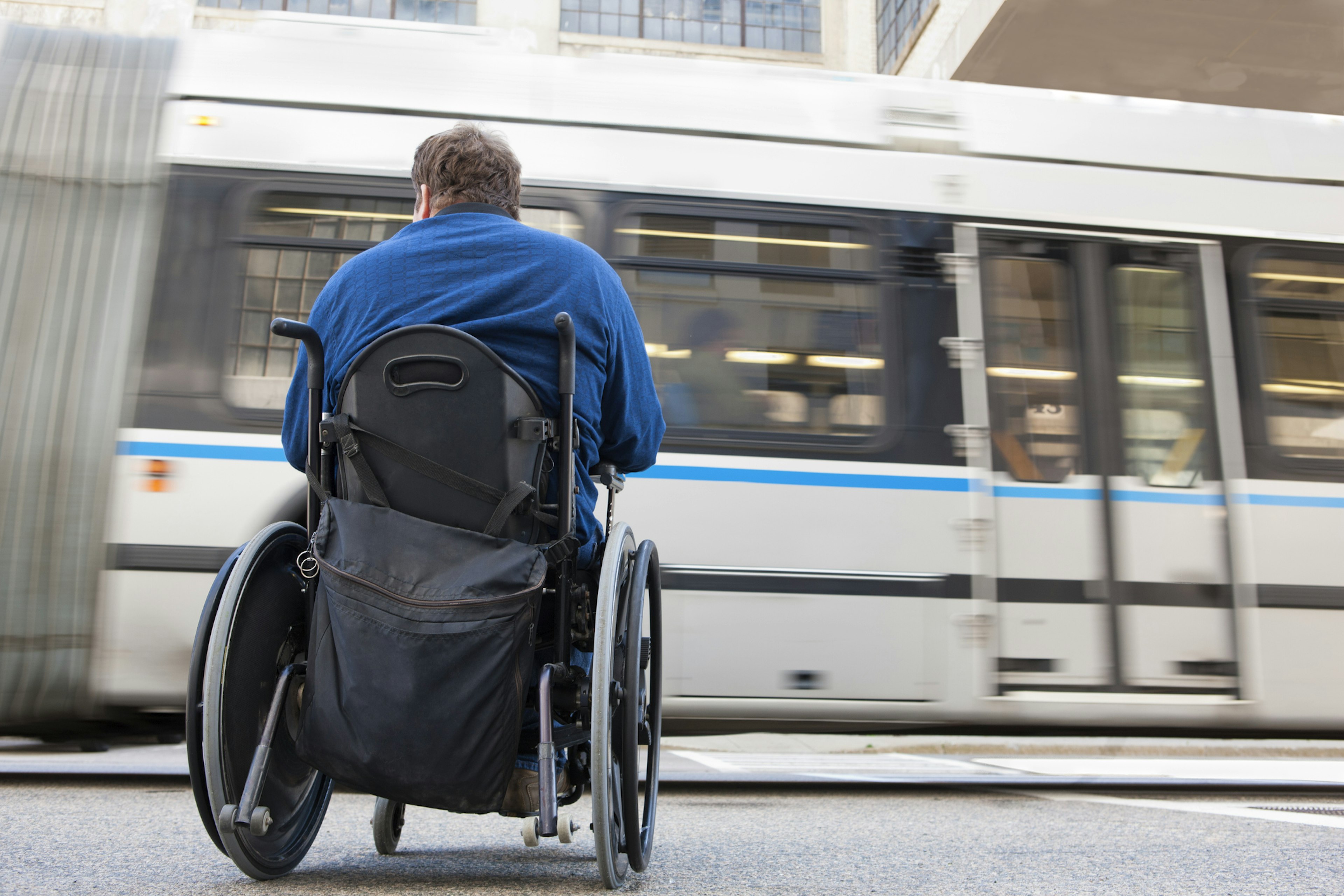 A wheelchair-user waits at a bus stop as a bus passes by