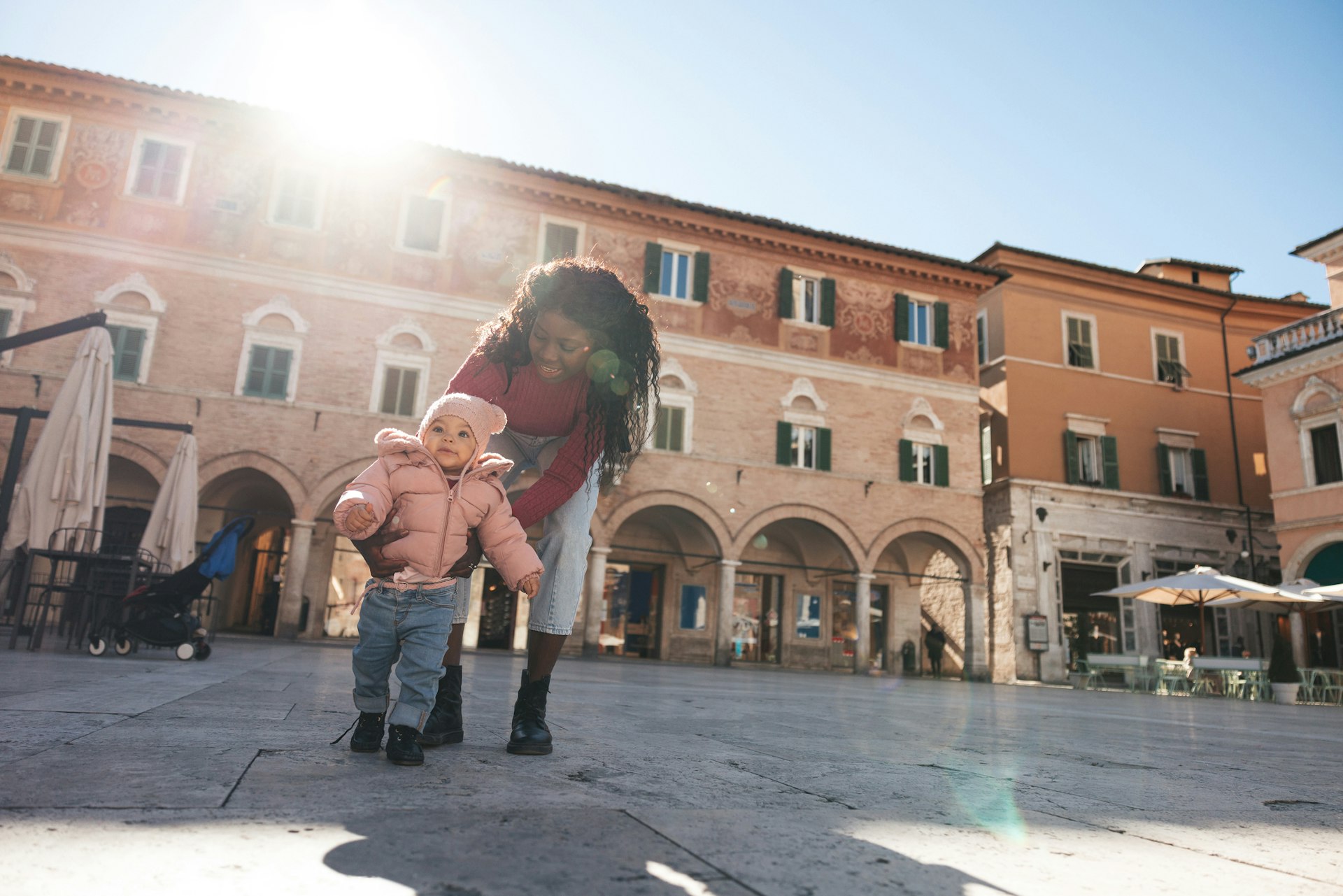 A mother walking with her baby girl in a city square in Italy