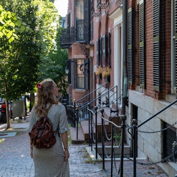 Young adult walking through the streets of Boston
1372001370
A young woman walking along a tree-lined residential street in Boston