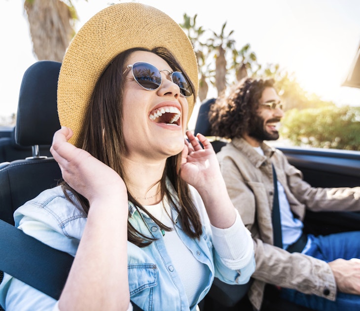 Happy couple driving convertible car enjoying summer vacation - Friends rent cabrio auto on holiday - Roadtrip, freedom, travel and transport rental service concept 1384618163 A smiling laughing couple driving a car in Spain