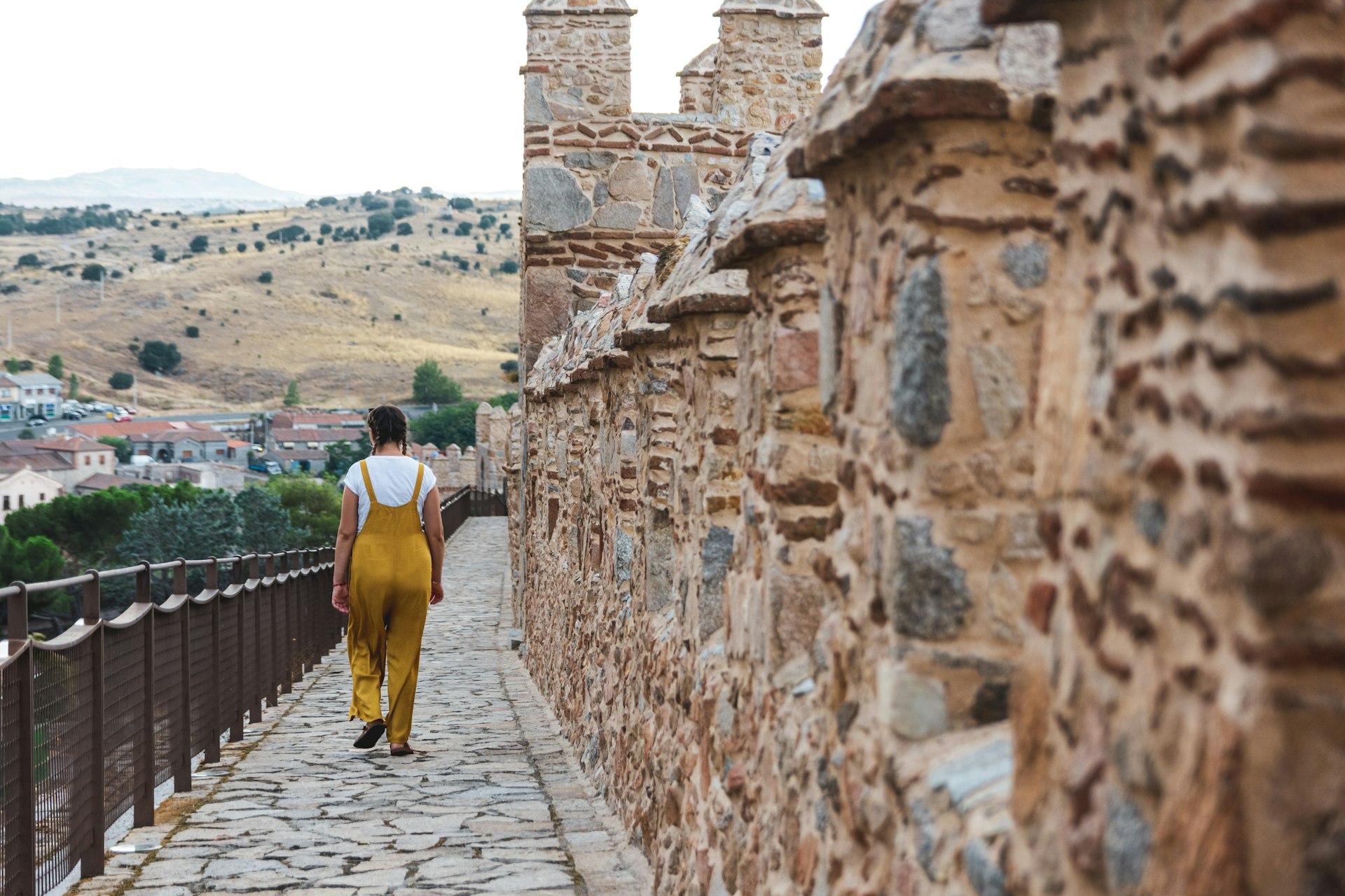 Young woman in dungarees walking along the medieval city walls of Avila