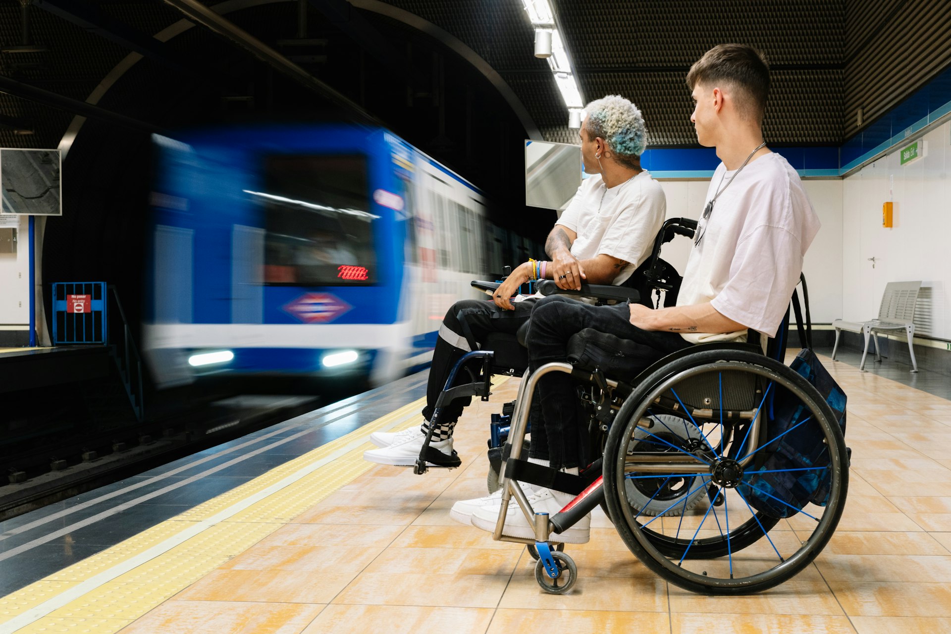 Horizontal panoramic view of young male friends in wheelchairs waiting for the train entering the station