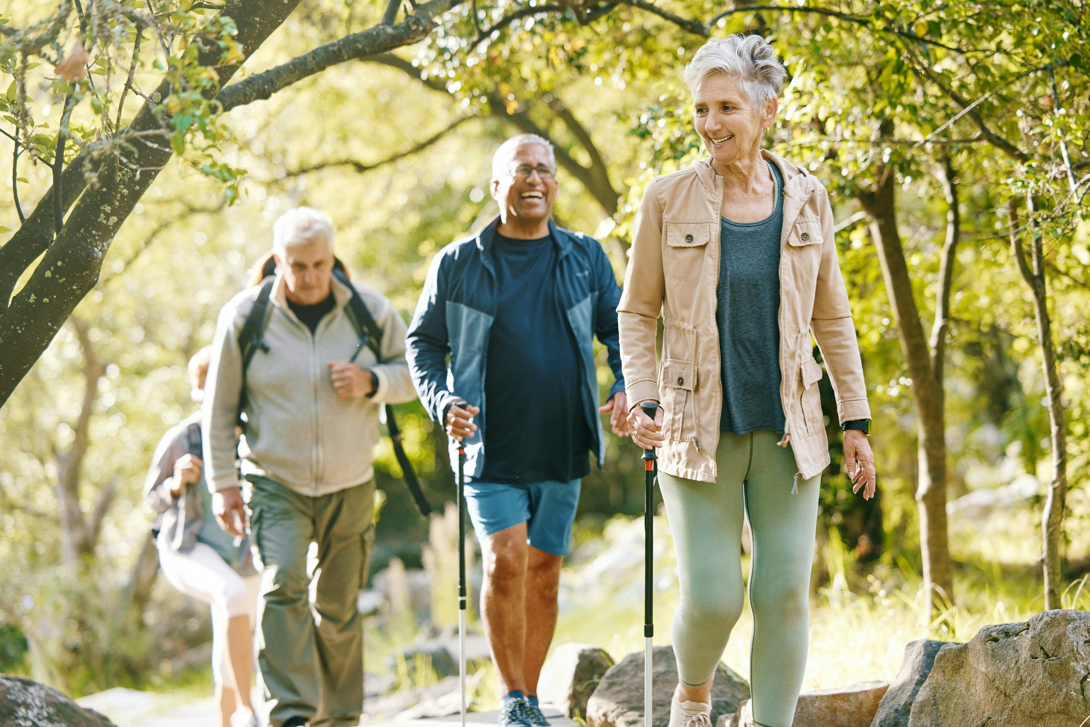 Three older friends smiling and laughing as they walk through a park in Boston