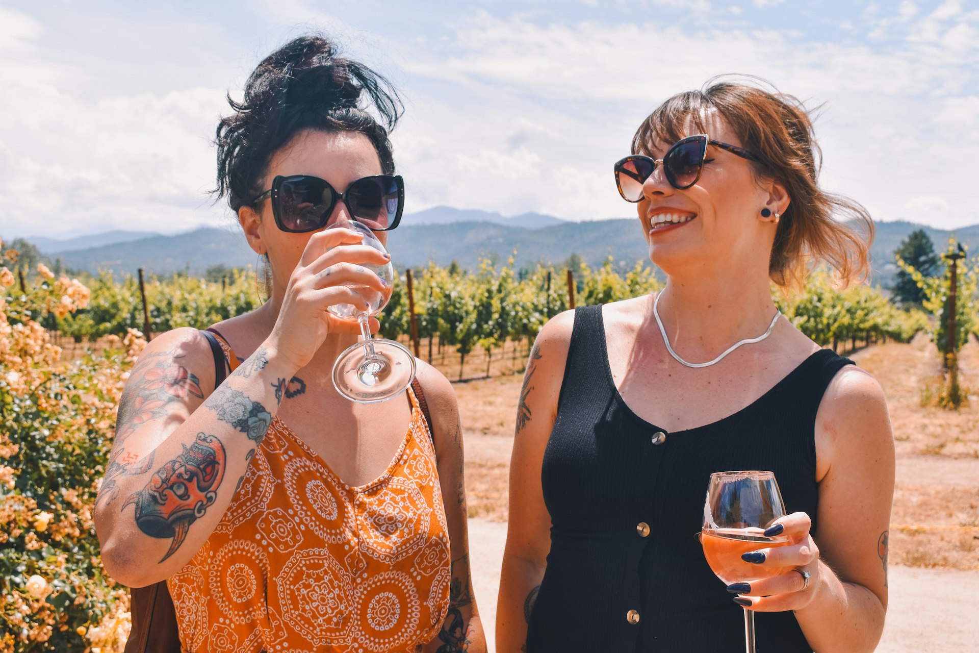 Two women drinking wine in the sunshine in a vineyard