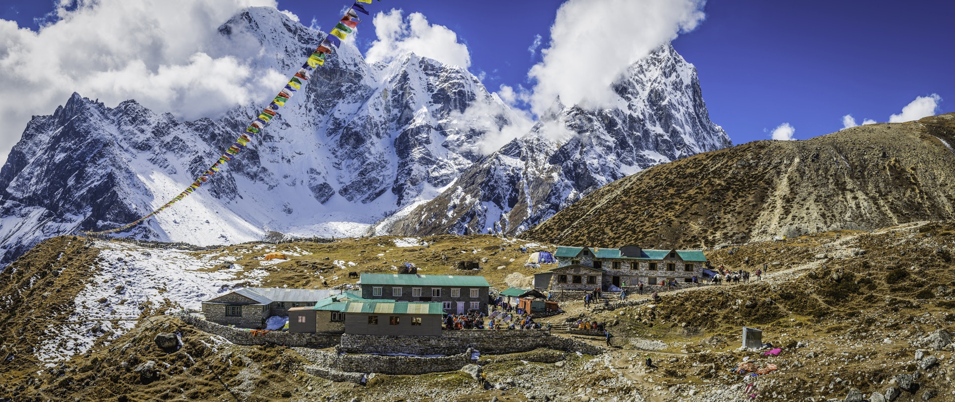 Crowds gather outside traditional teahouses (lodgings) on the trail to Everest Base Camp with colorful flags fluttering in the breeze