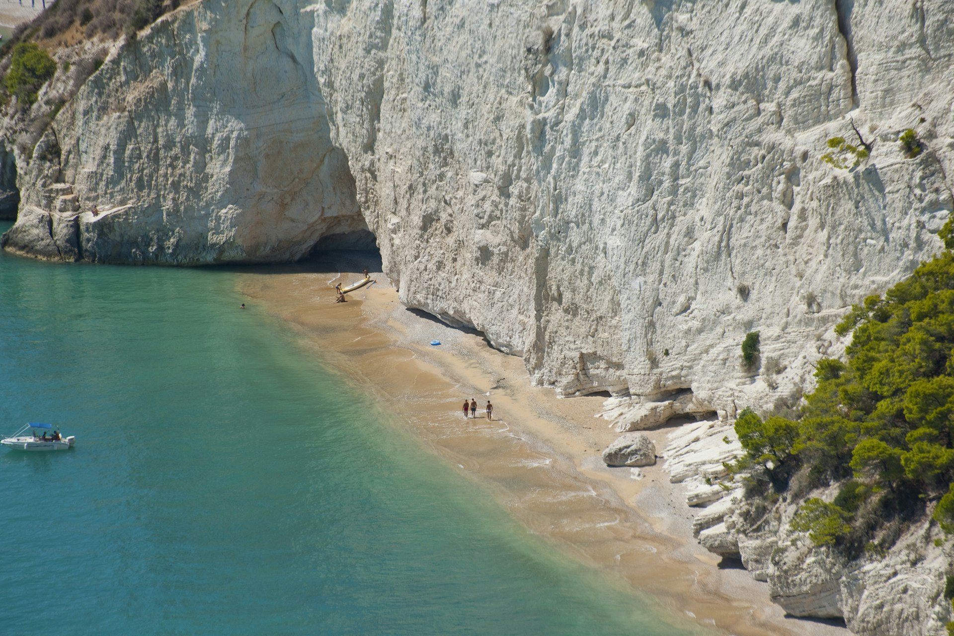 Three people walk along a beach backed by vast white cliffs