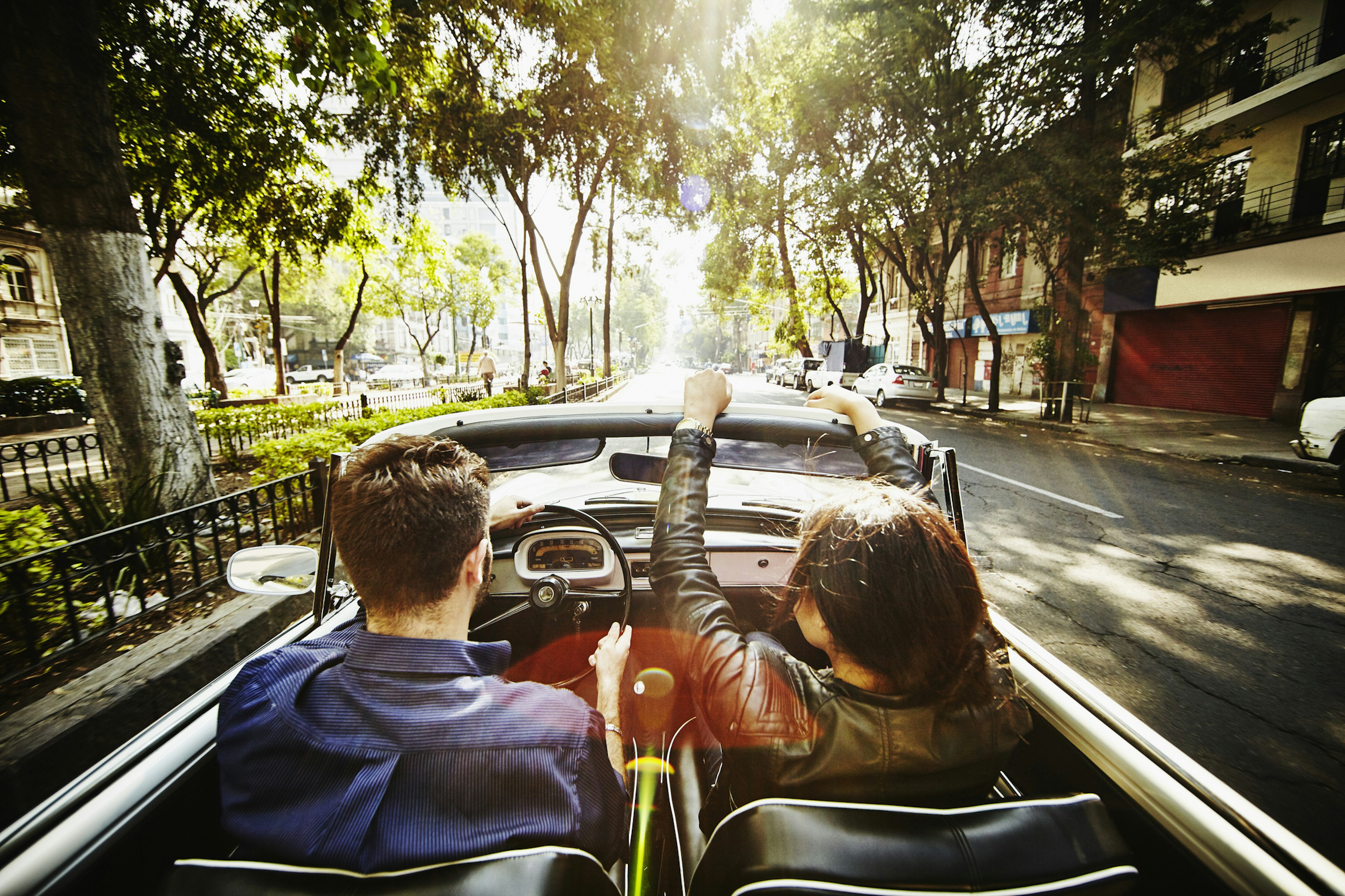 A couple drive in a convertible car in a city at sunrise