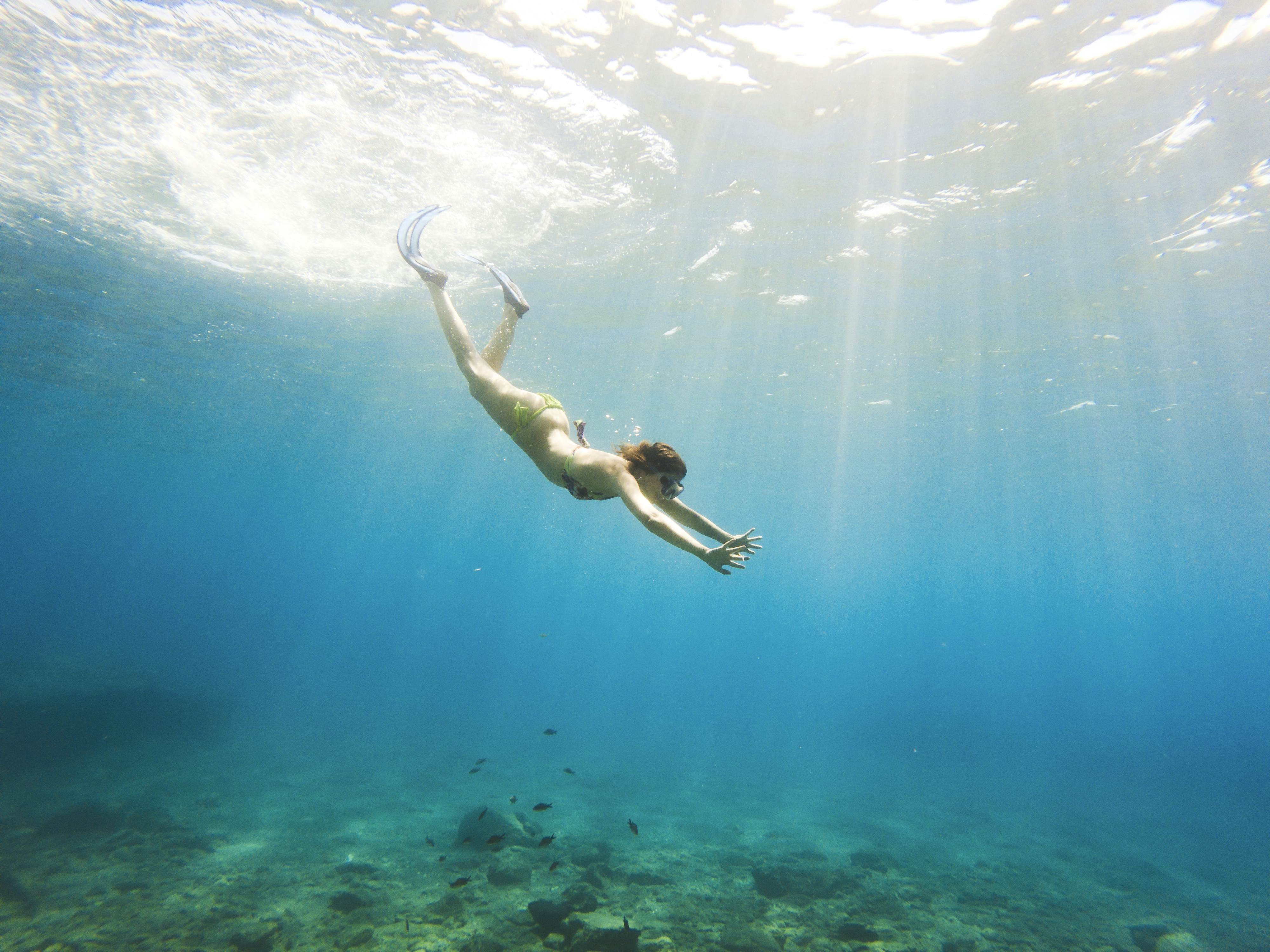 An underwater view of a woman diving in the crystalline sea off Milos, Greece